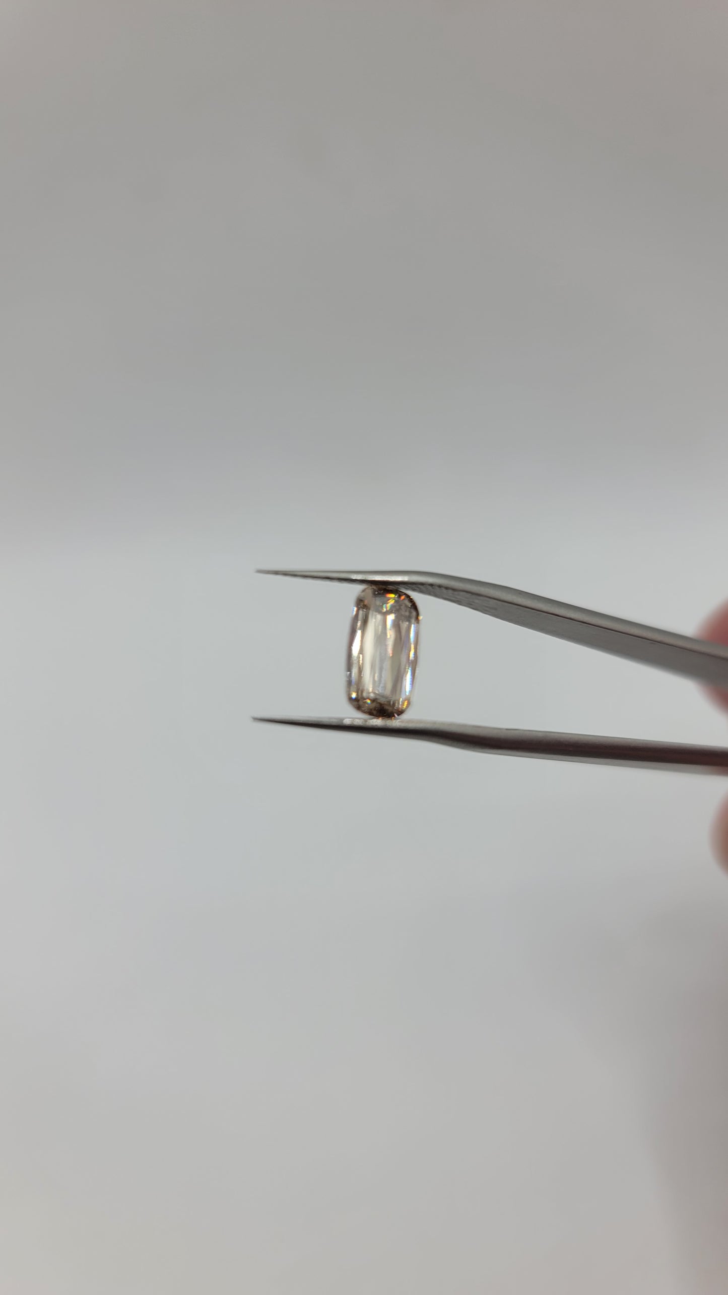 A lab grown crisscut diamond held between metal tweezers against a plain light gray background.