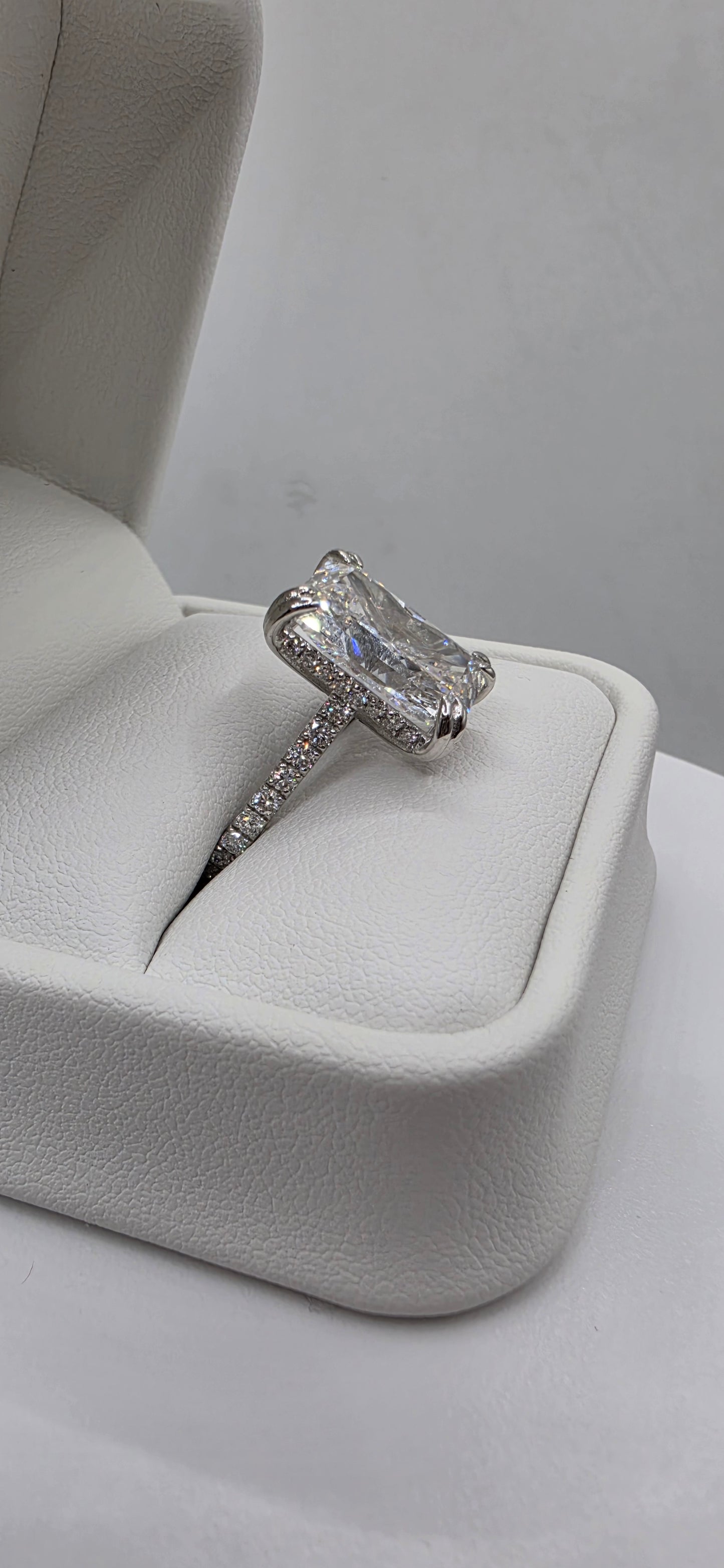 Diamond ring on a white cushioned stand against a neutral background