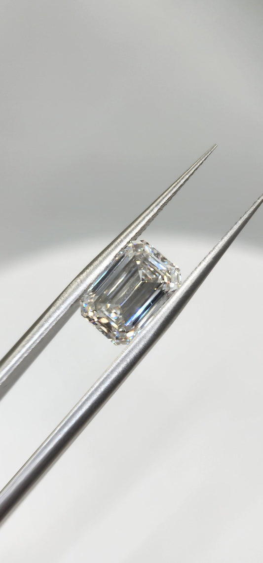 Emerald-cut diamond on a silver prong setting against a light gray background