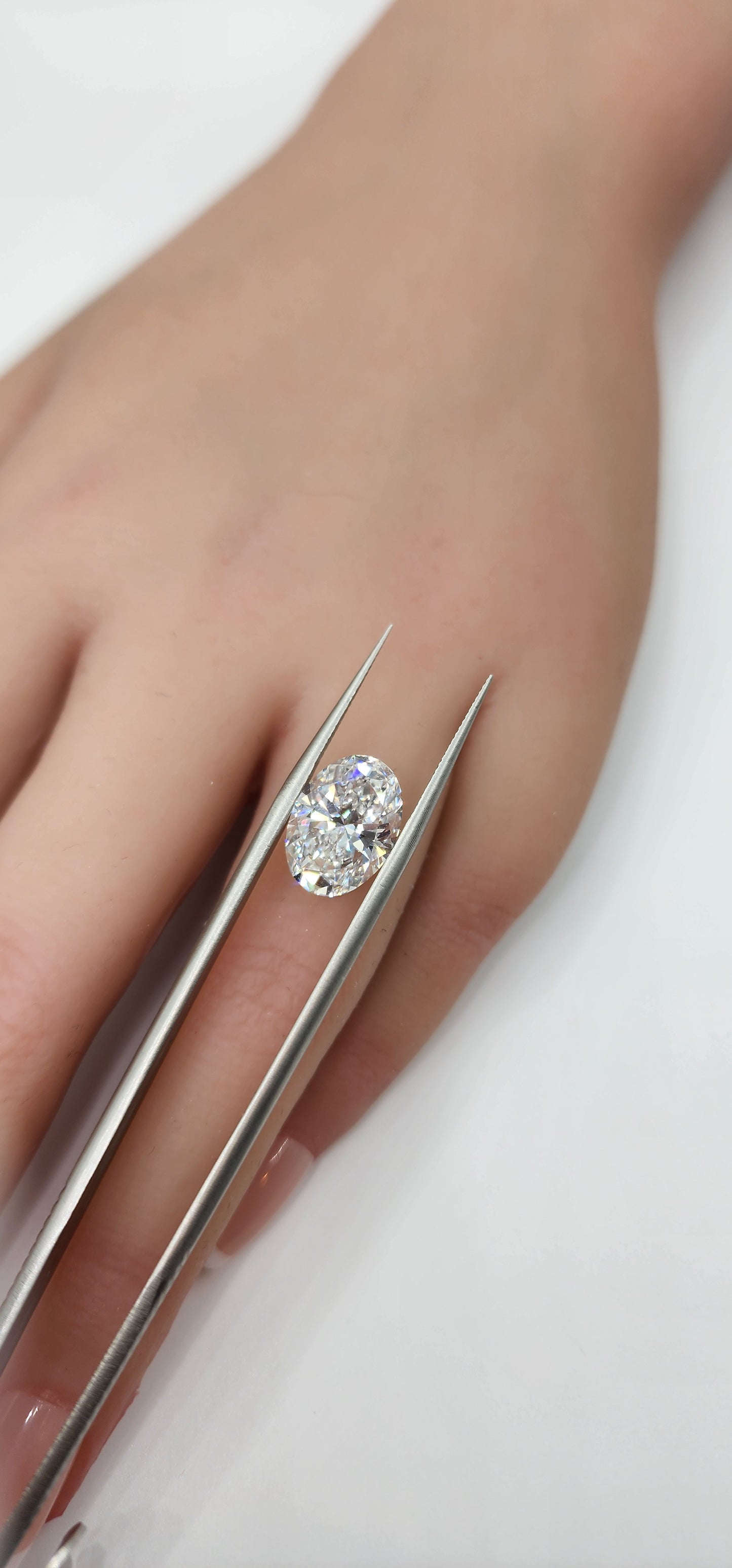 Diamond held by tweezers over a hand with a white background