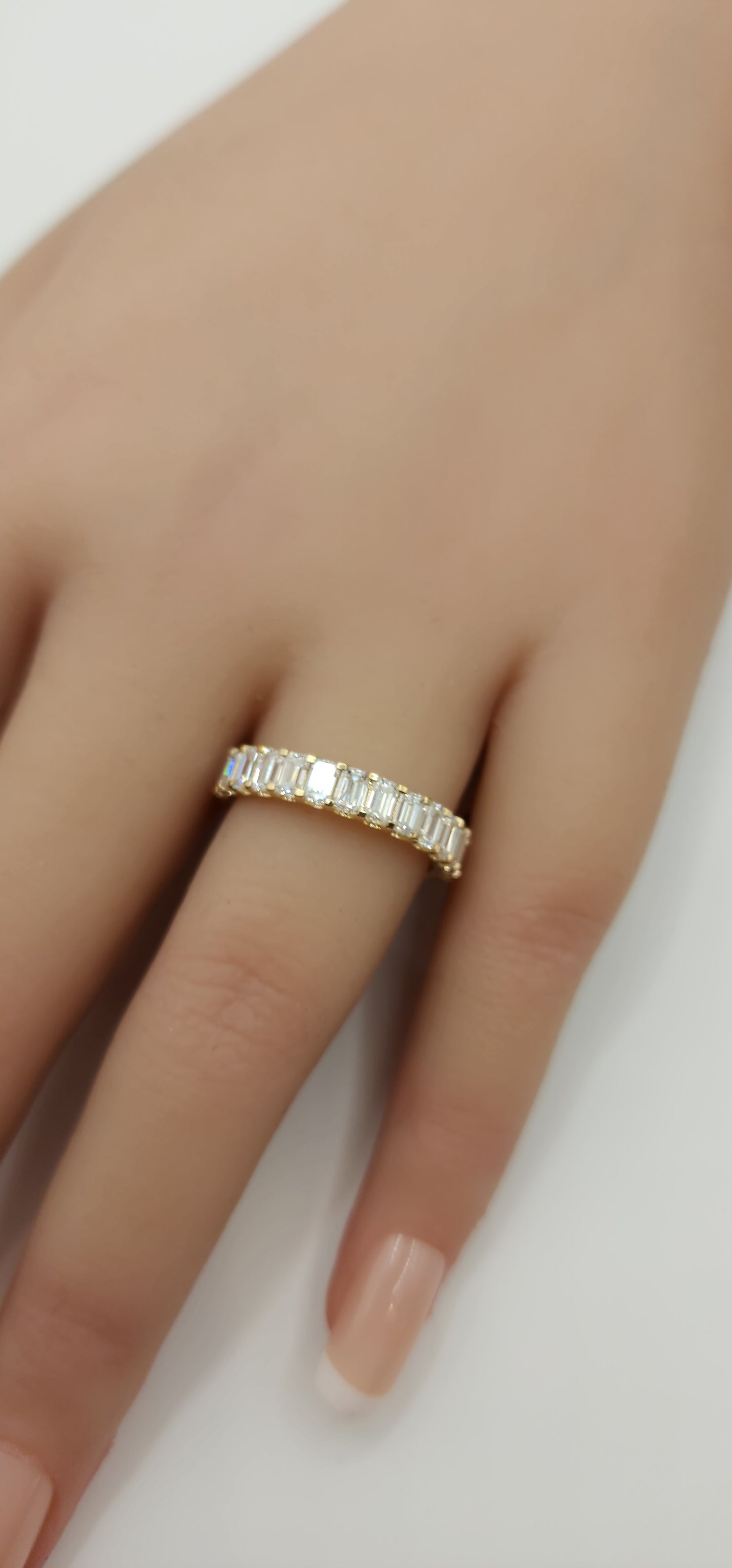 Gold ring with diamonds on a finger against a neutral background