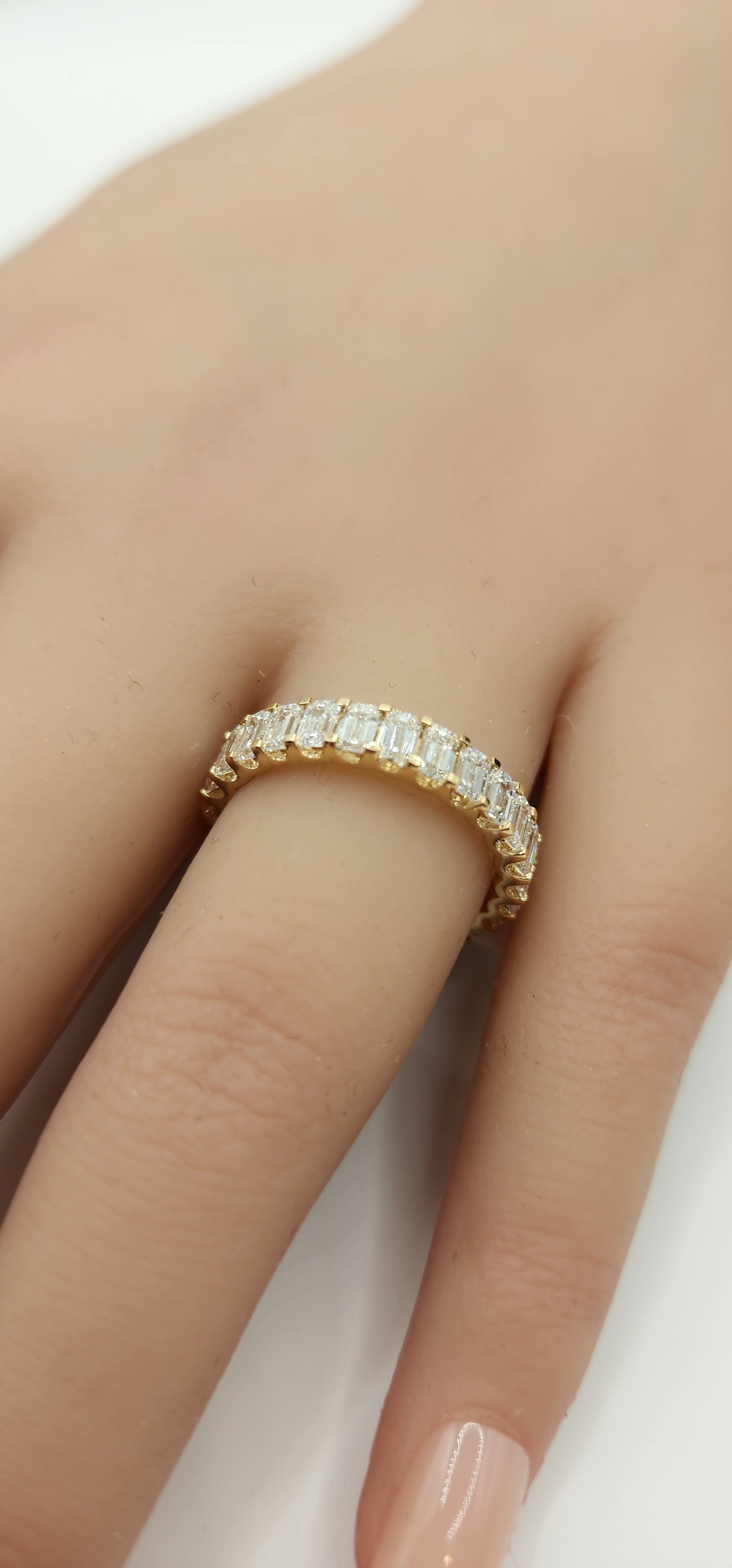 Gold ring with diamonds on a finger against a neutral background