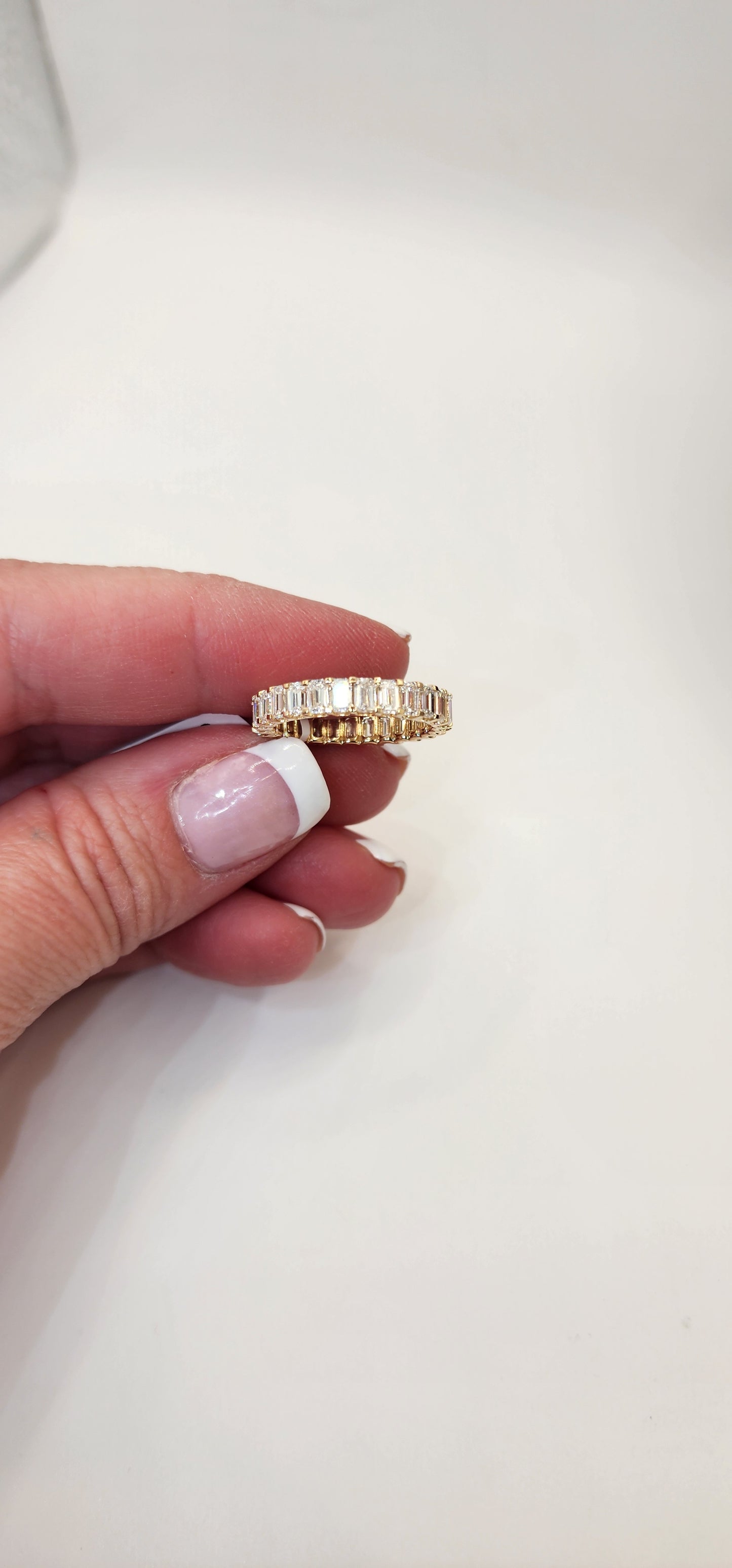 Gold and emerald cut diamond ring held between fingers against a plain background