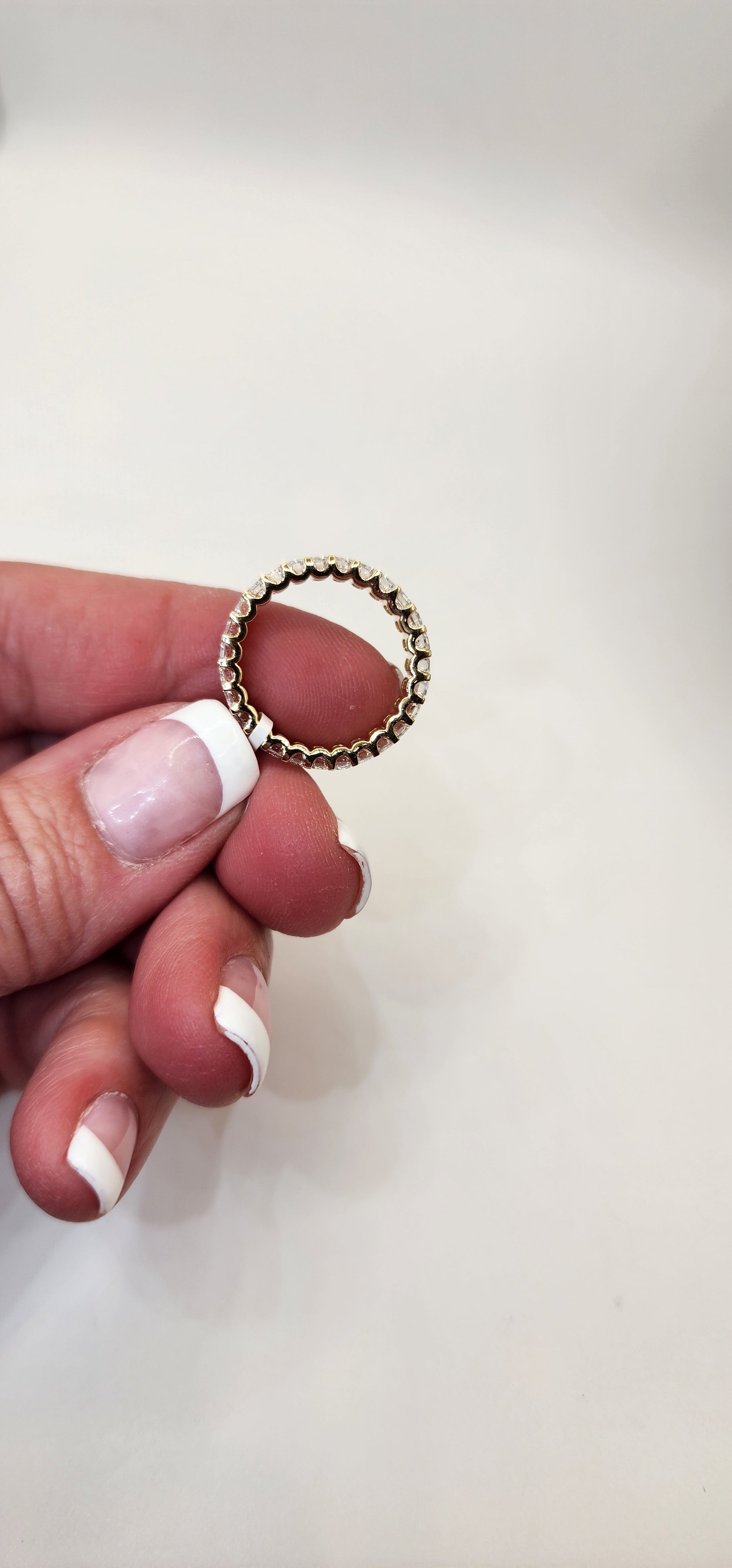 Gold ring held between fingers with a plain background