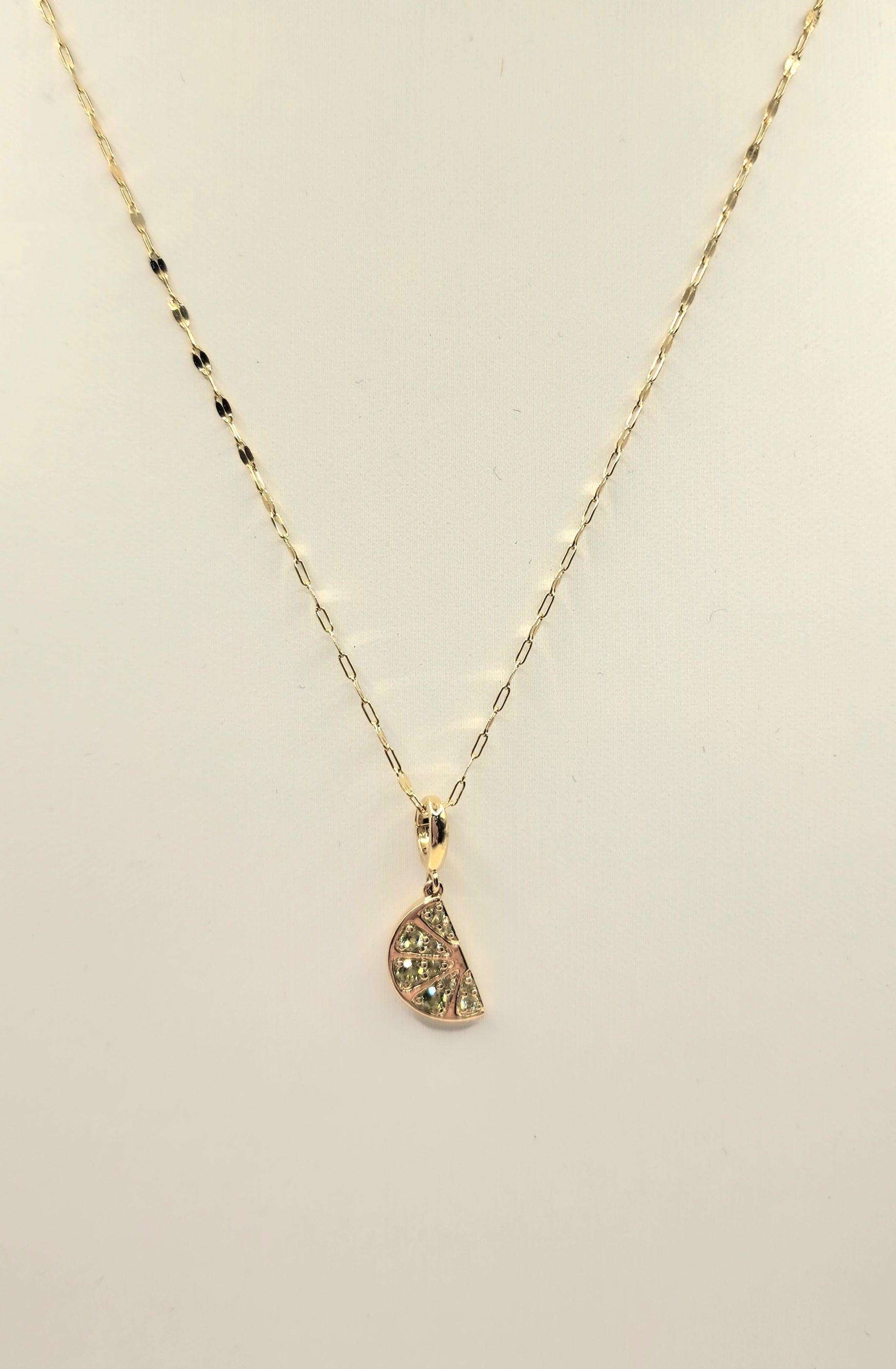 Gold necklace with a lime wedge-shaped pendant on a beige background