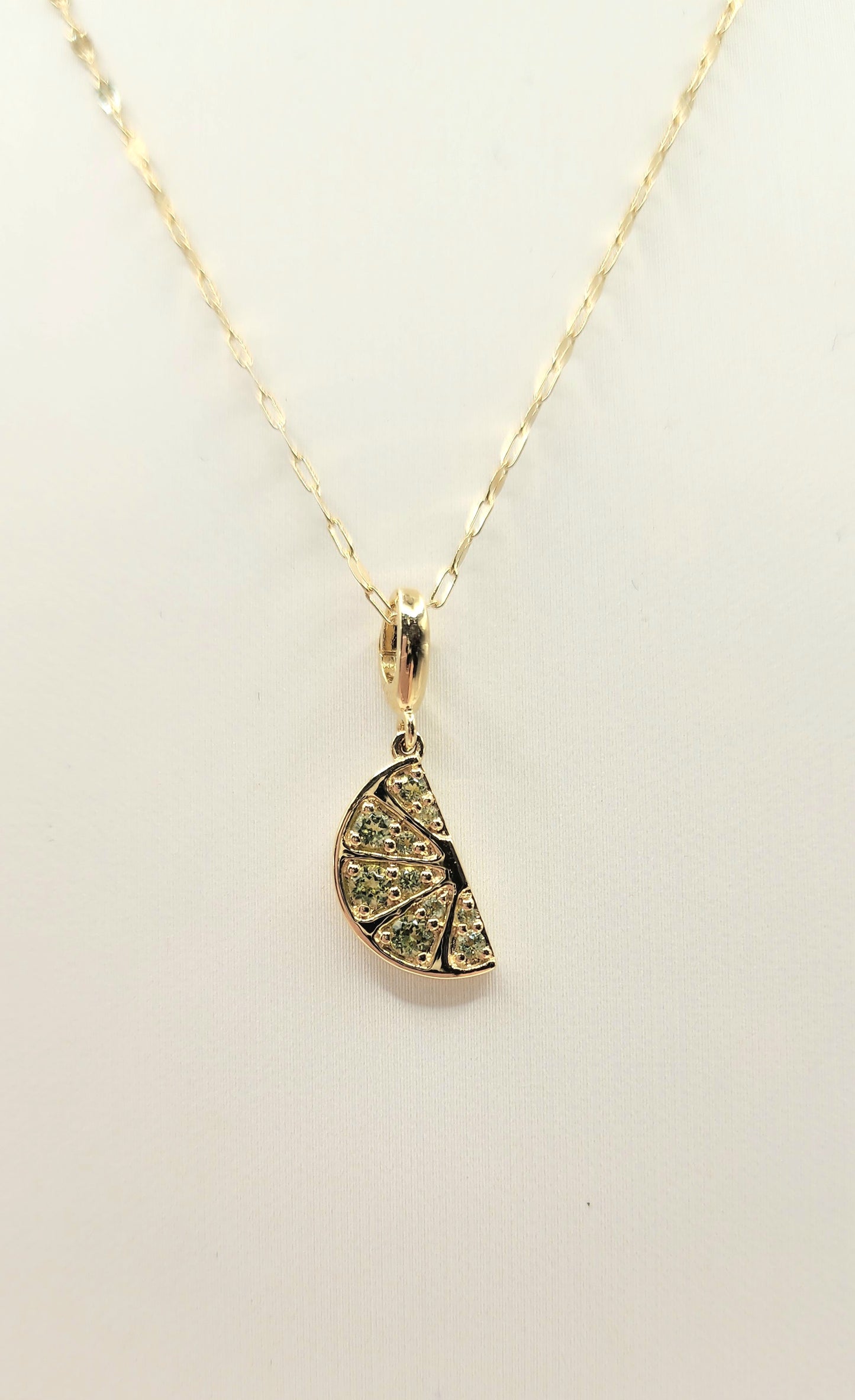 Gold necklace with a lime wedge-shaped pendant on a beige background
