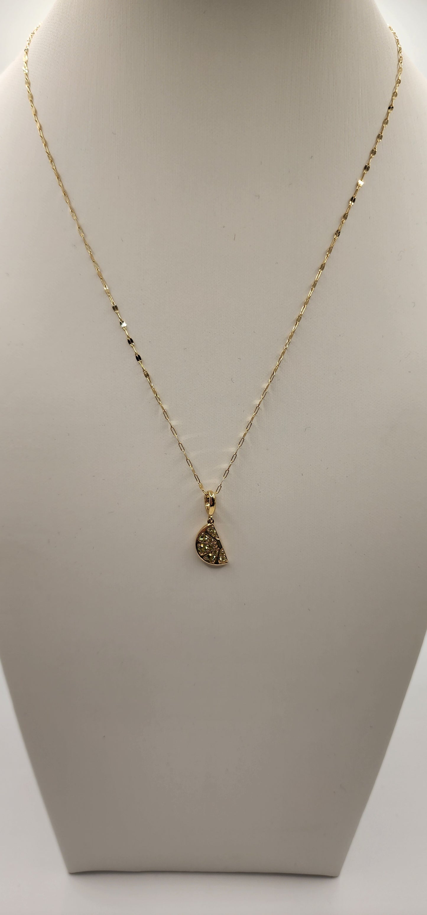 Gold necklace with a lime wedge-shaped pendant on a beige background
