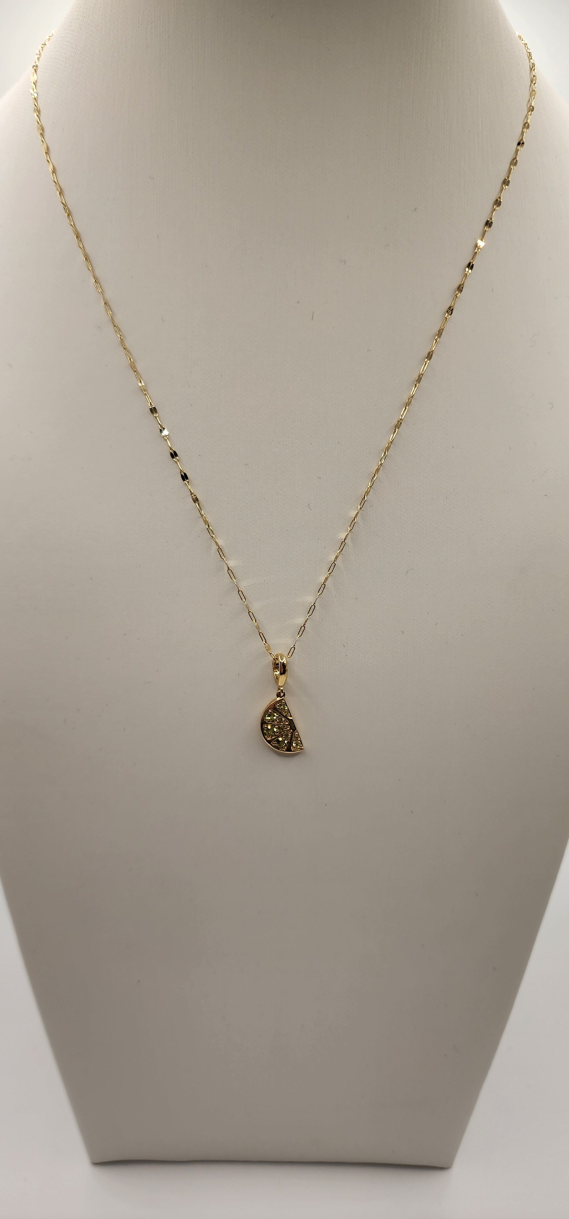Gold necklace with a lime wedge-shaped pendant on a beige background