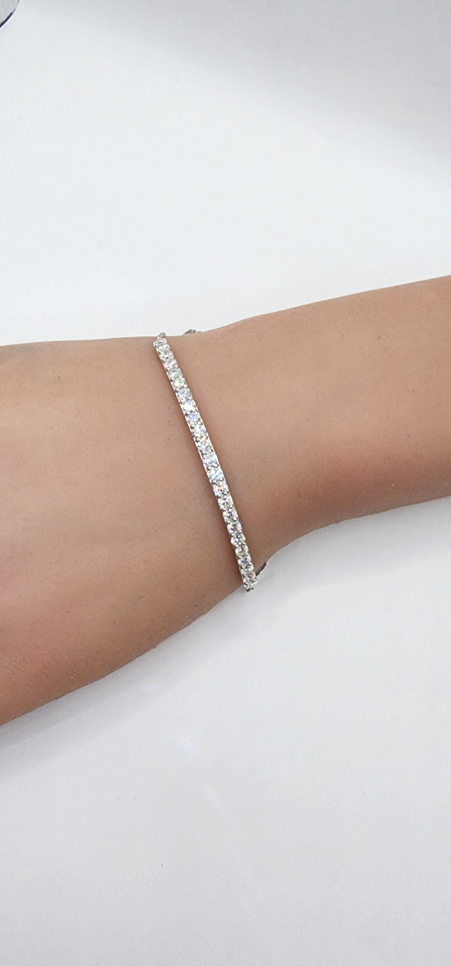 White gold and diamond bracelet on a persons wrist against a white back drop