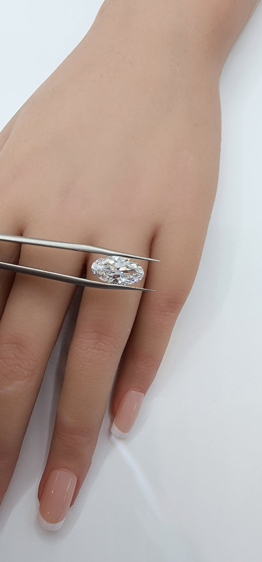 Diamond ring on a hand with tweezers holding it, against a white background