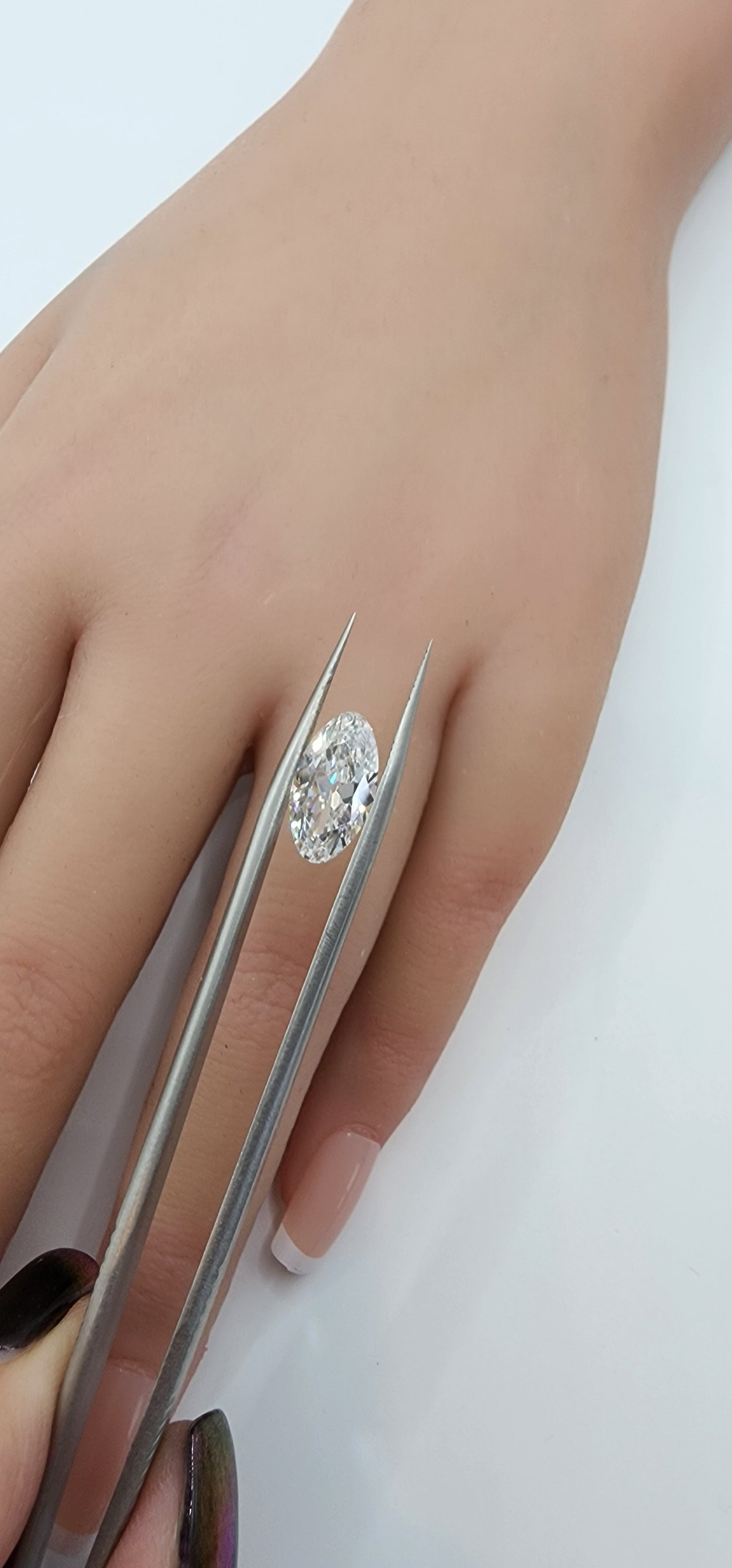Diamond held by tweezers with a hand on a white background