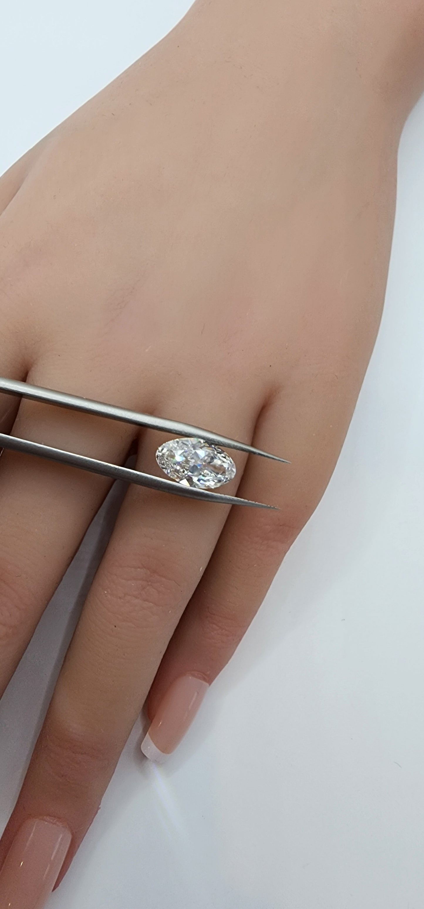 Diamond being held between tweezers with a hand wearing a diamond ring on a white background