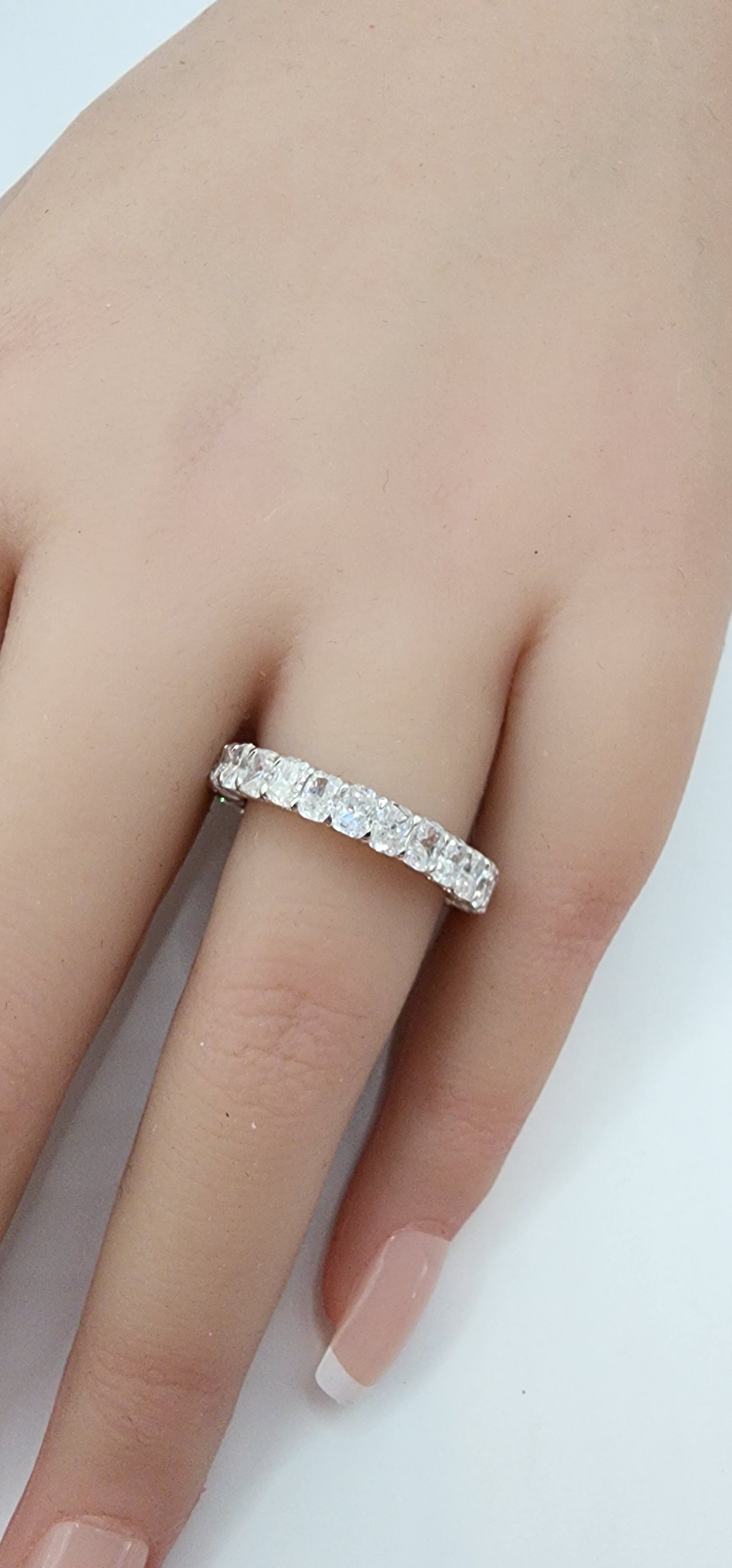 White Gold ring with clear stones on a finger against a white background