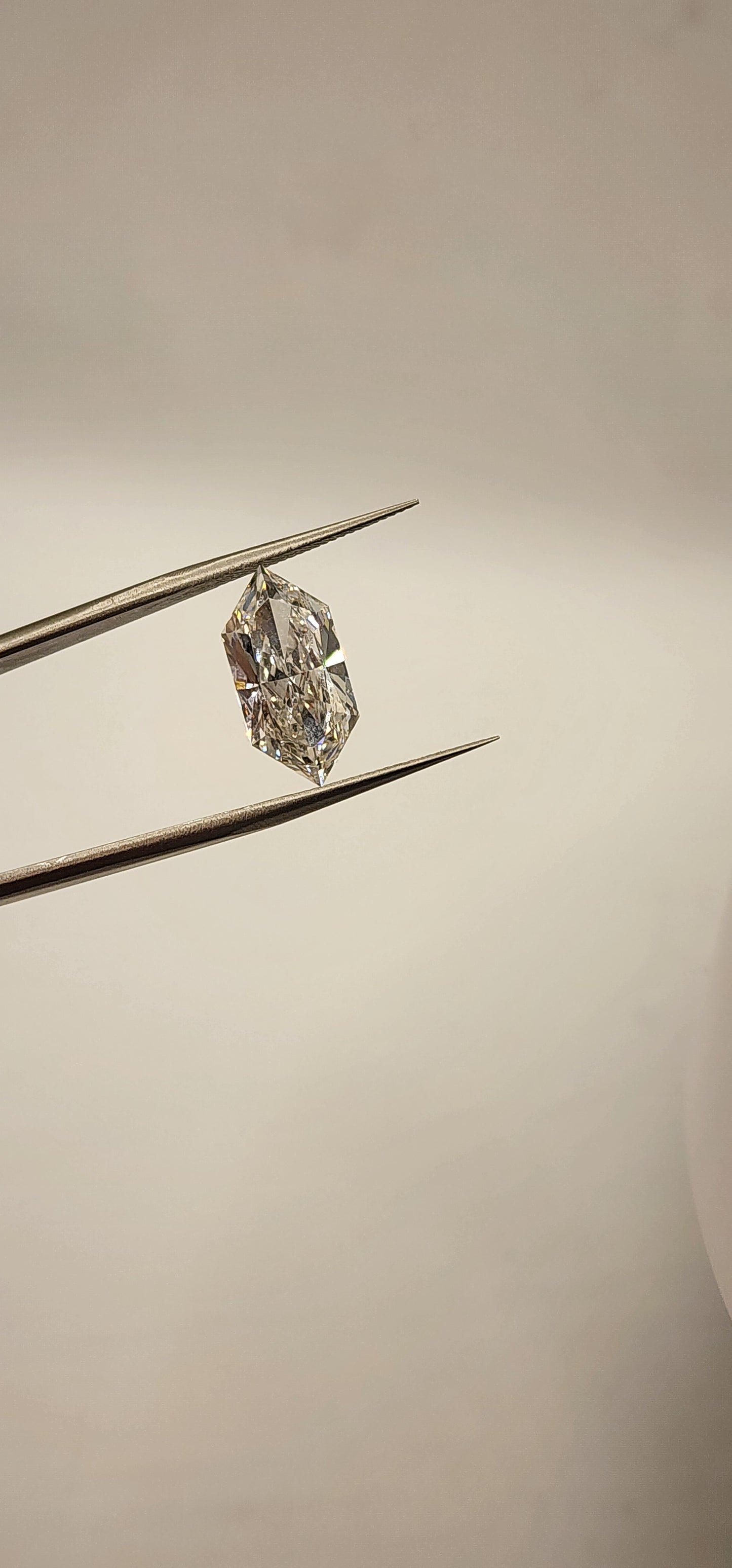 Diamond in tweezers in front of a grey background