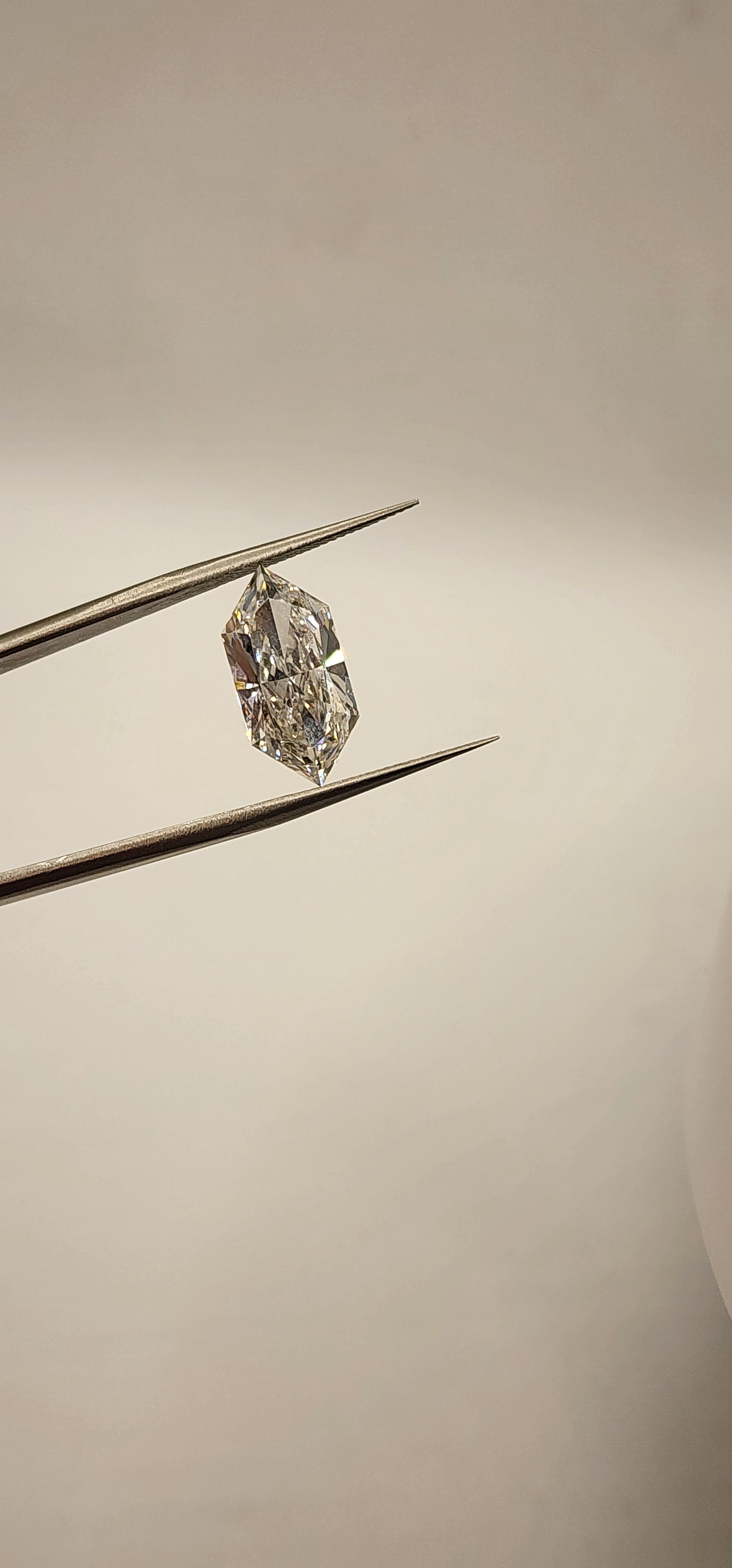 Diamond in tweezers in front of a grey background