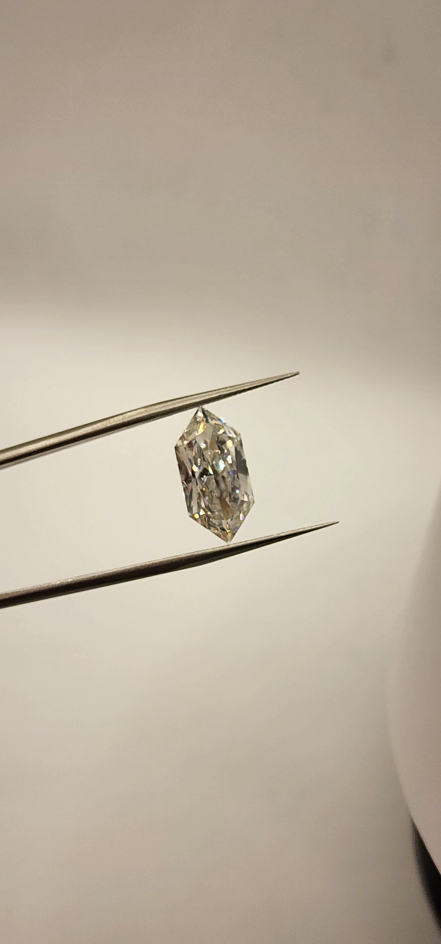 Diamond in tweezers in front of a grey background