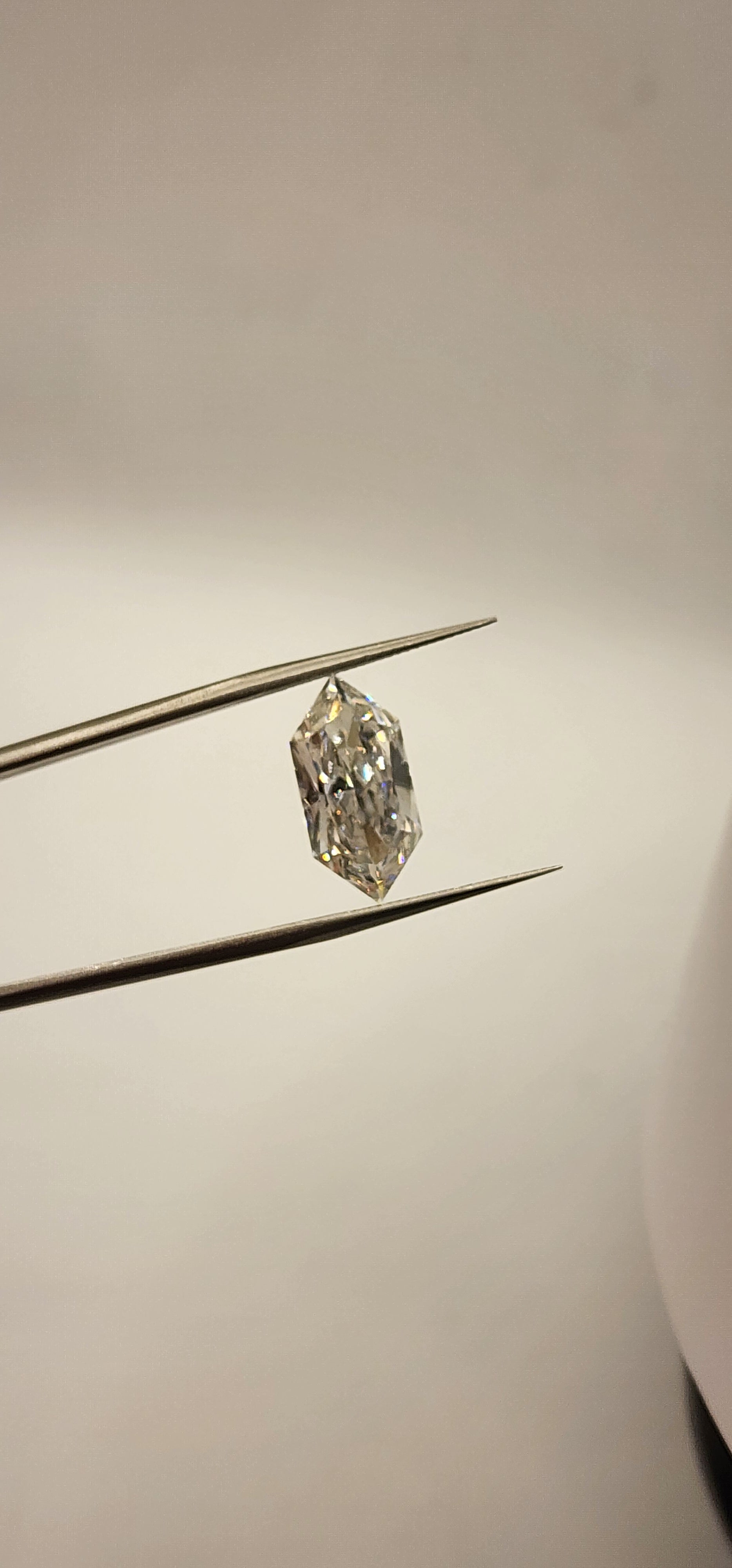 Diamond in tweezers in front of a grey background