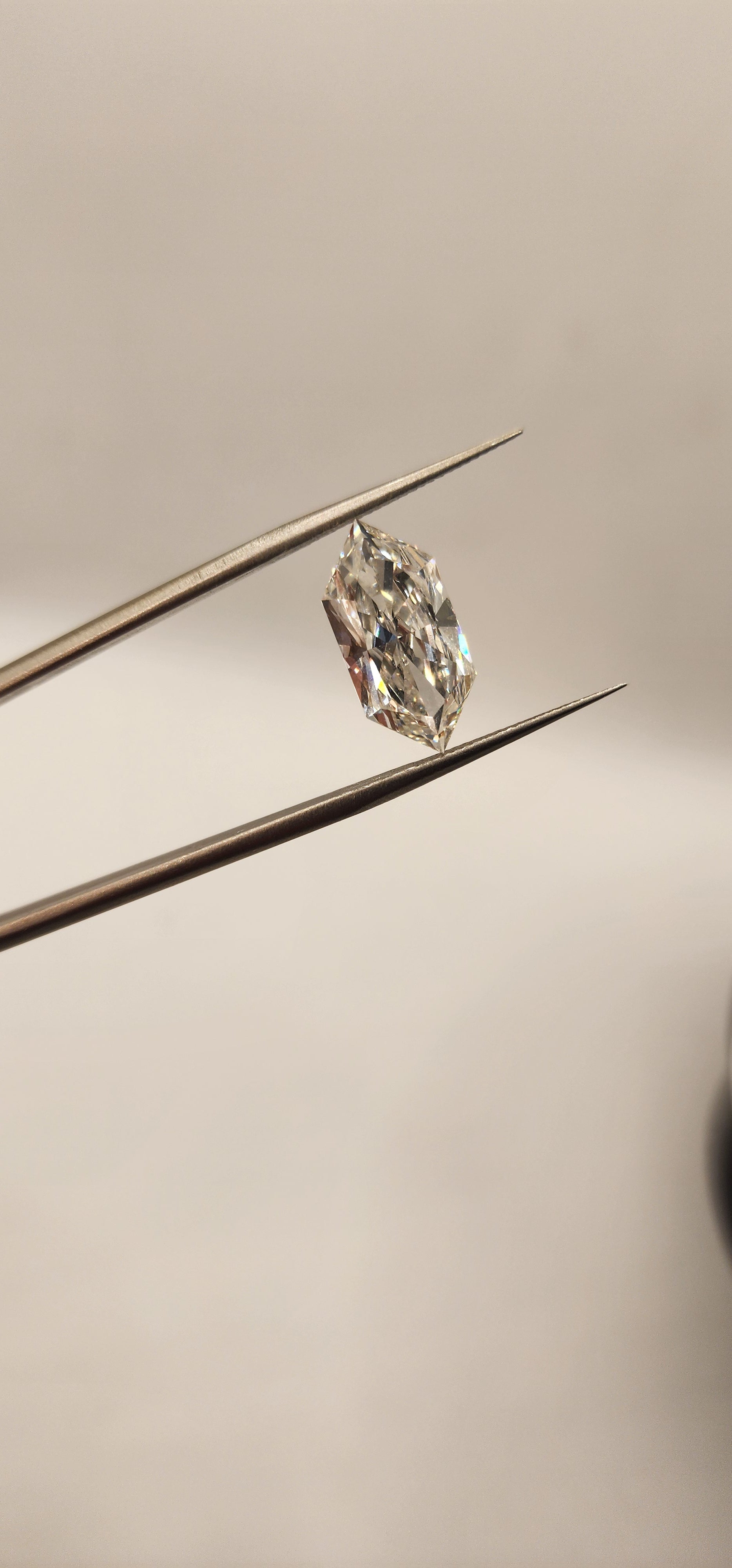 Diamond in tweezers in front of a grey background