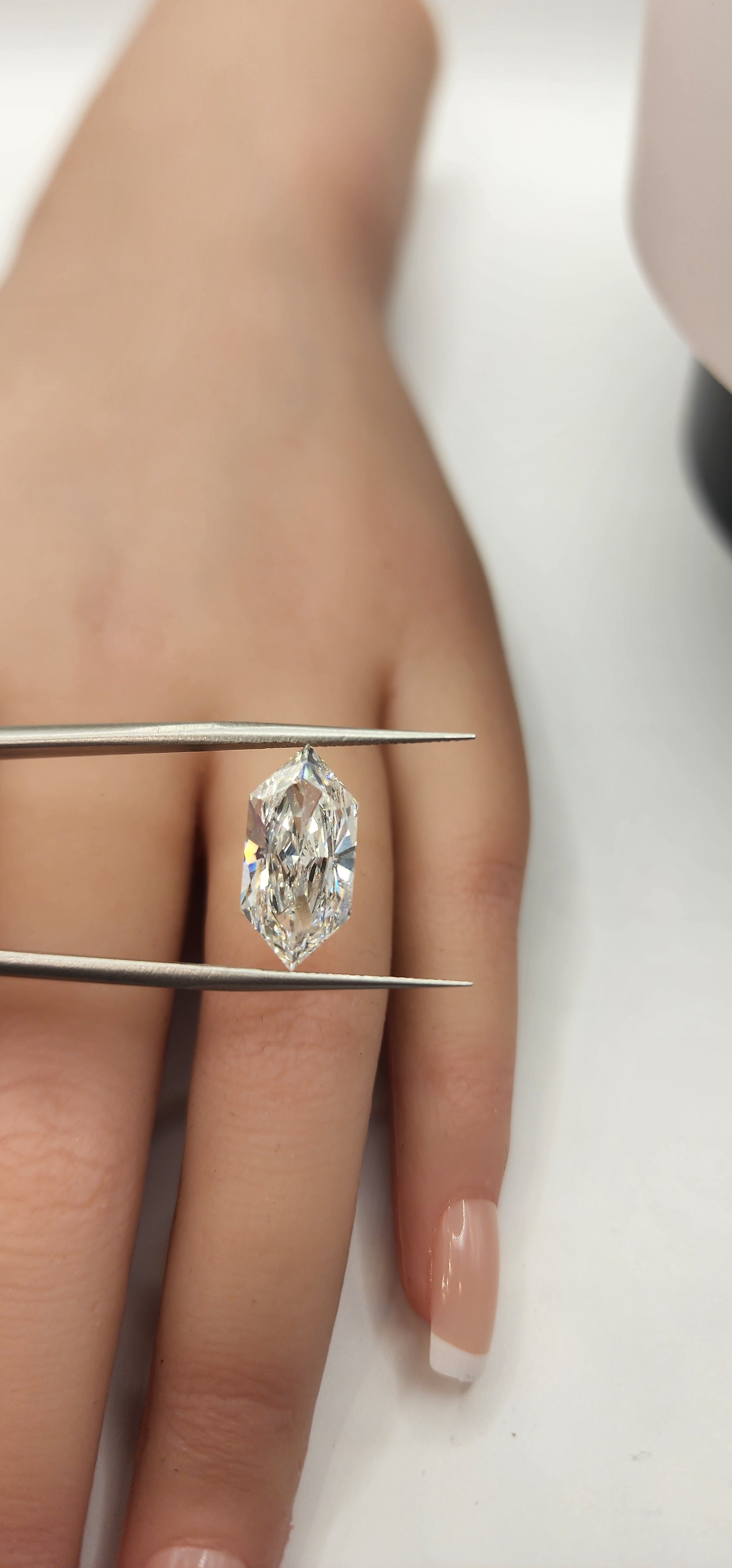 Diamond inside tweezers in front of a hand on  a white background