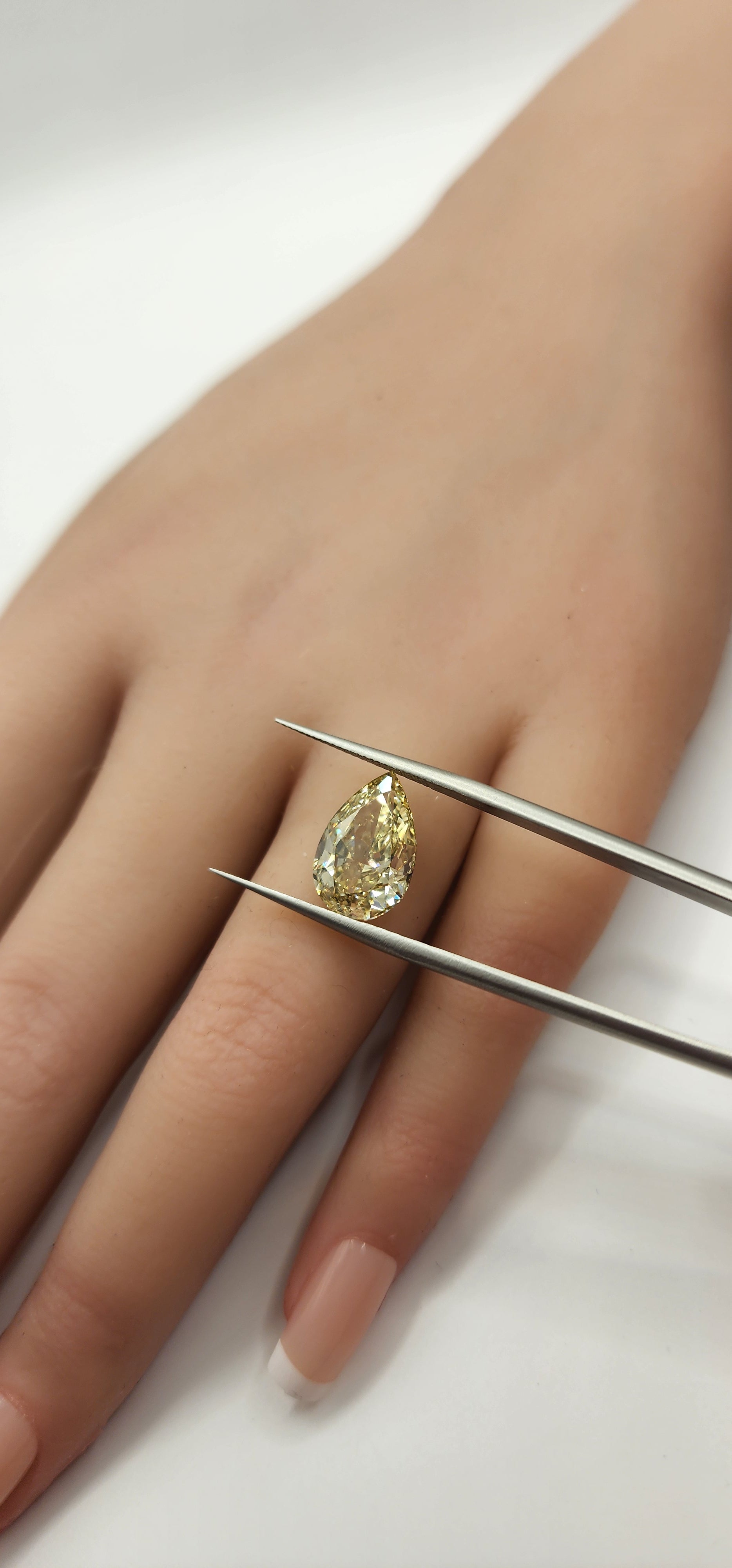 Yellow pear diamond being held by tweezers in front of a hand by a grey backdrop