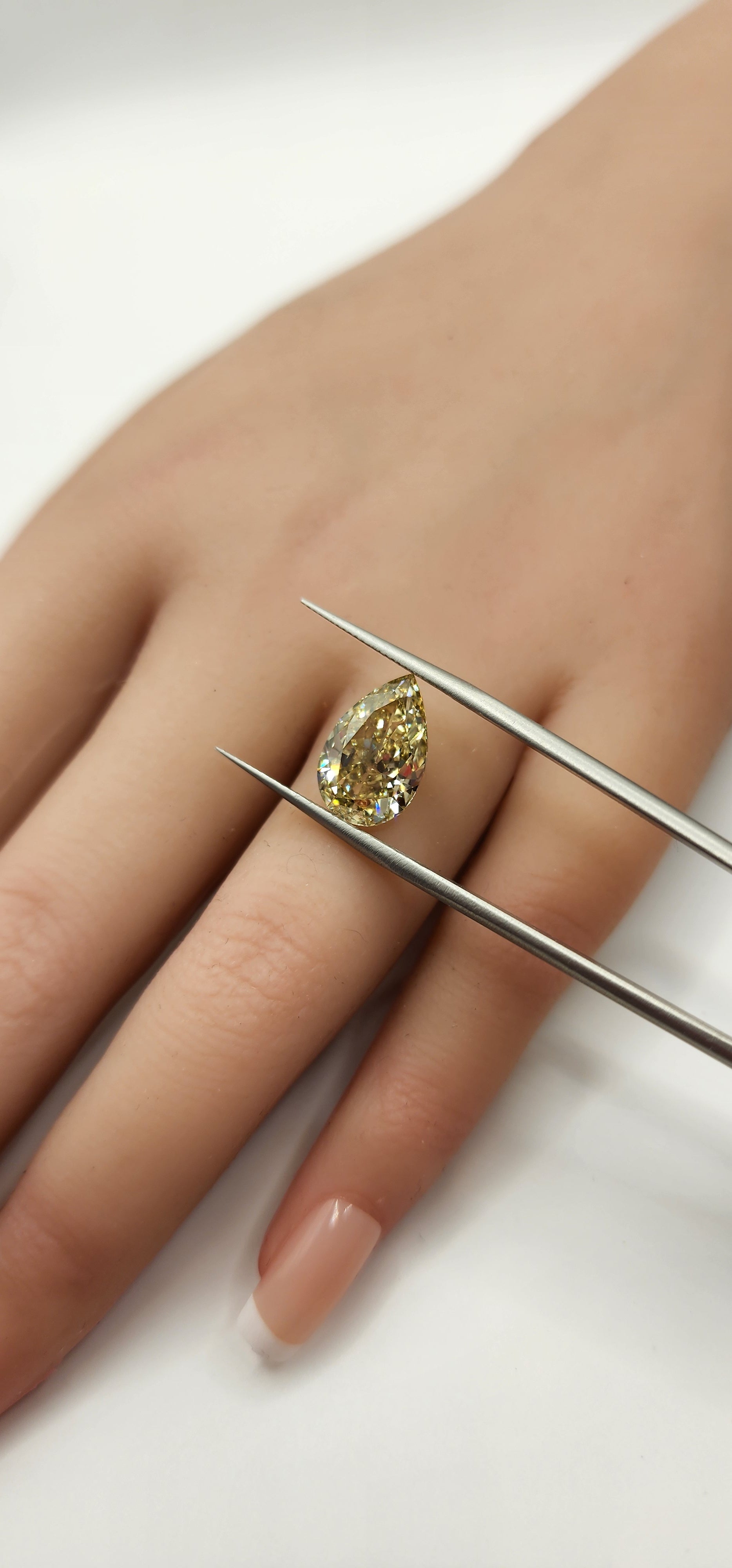Yellow pear diamond being held by tweezers in front of a hand by a grey backdrop