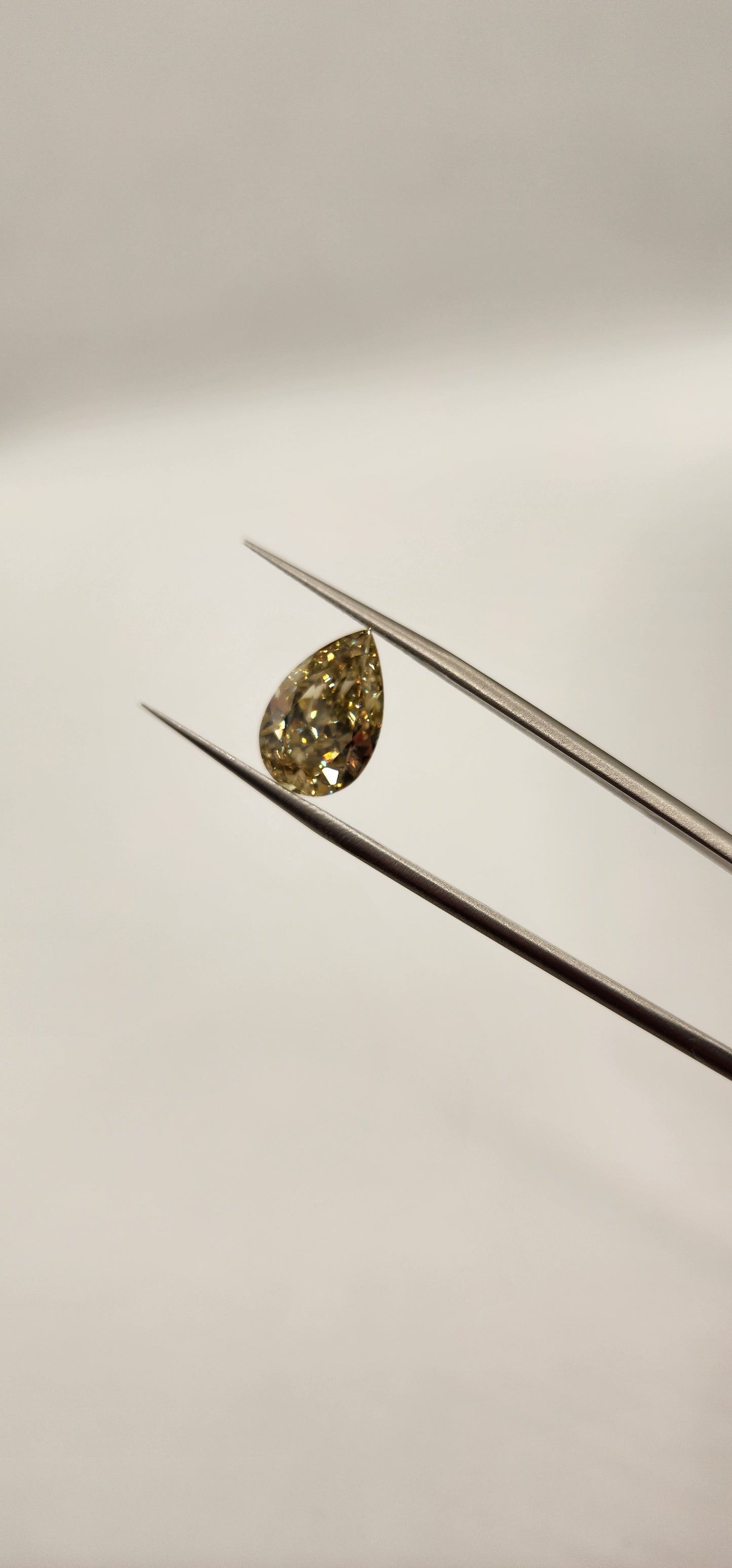 Yellow diamond being held by tweezers in front of grey background