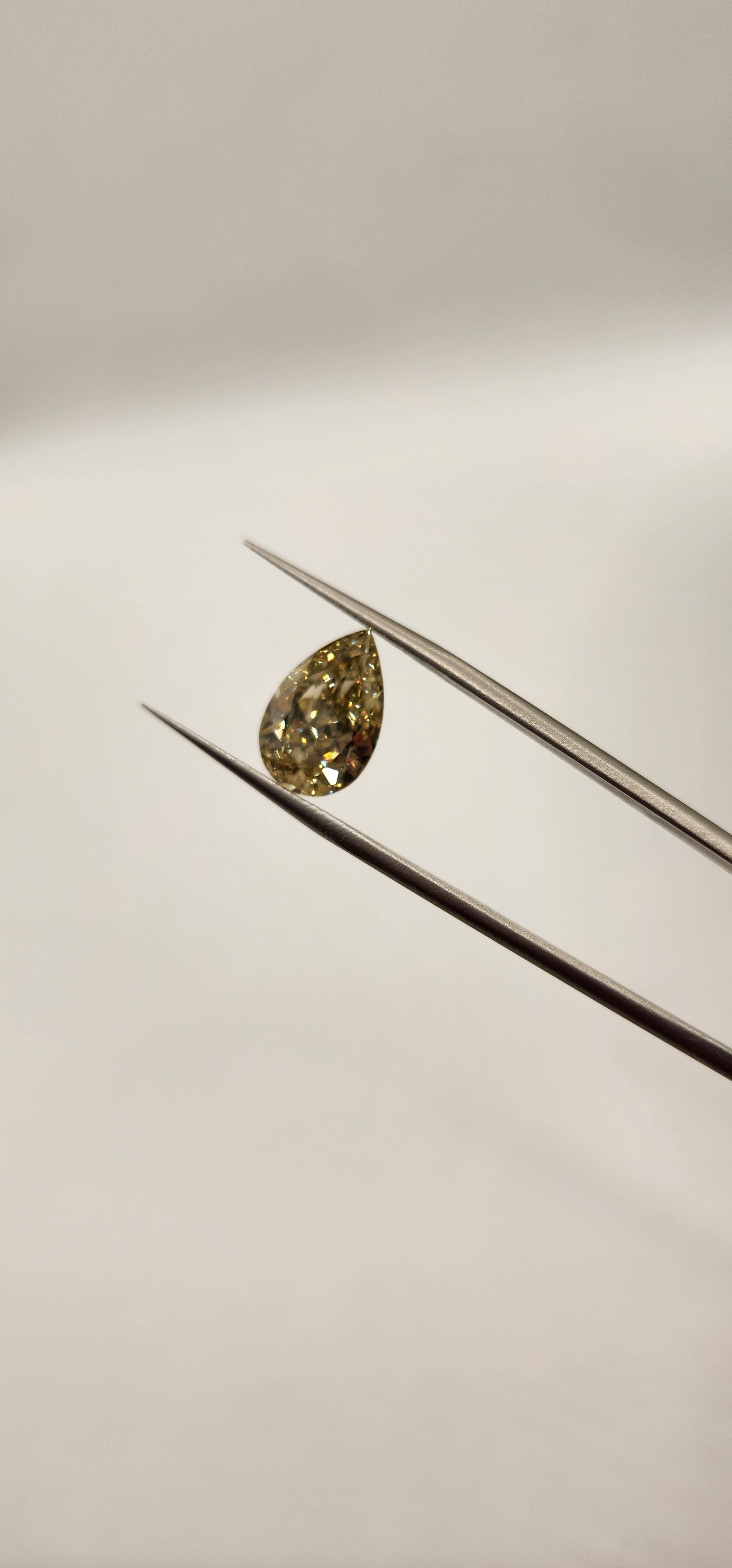 Yellow diamond being held by tweezers in front of grey background
