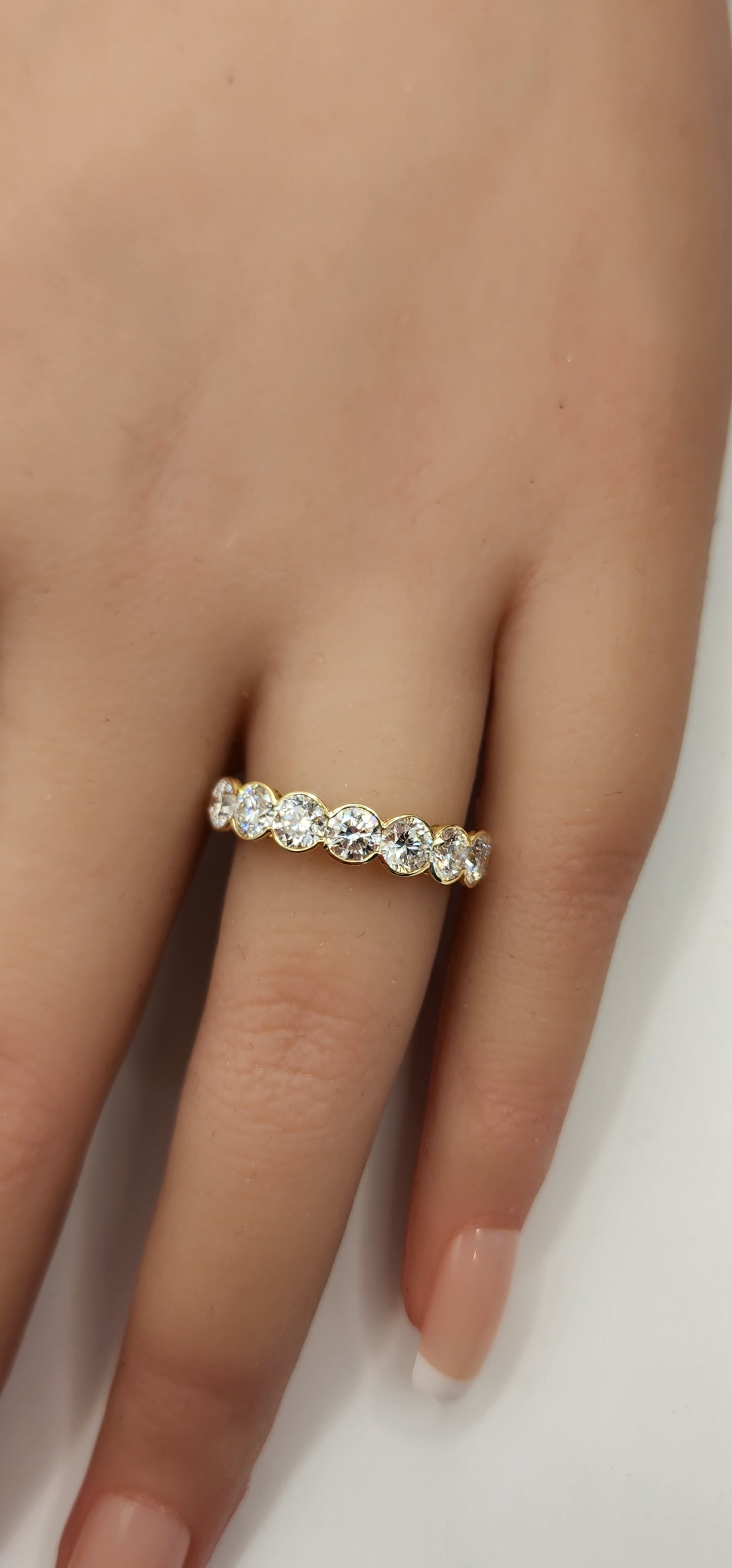 Round diamond and yellow gold ring on a hand in front of white backdrop