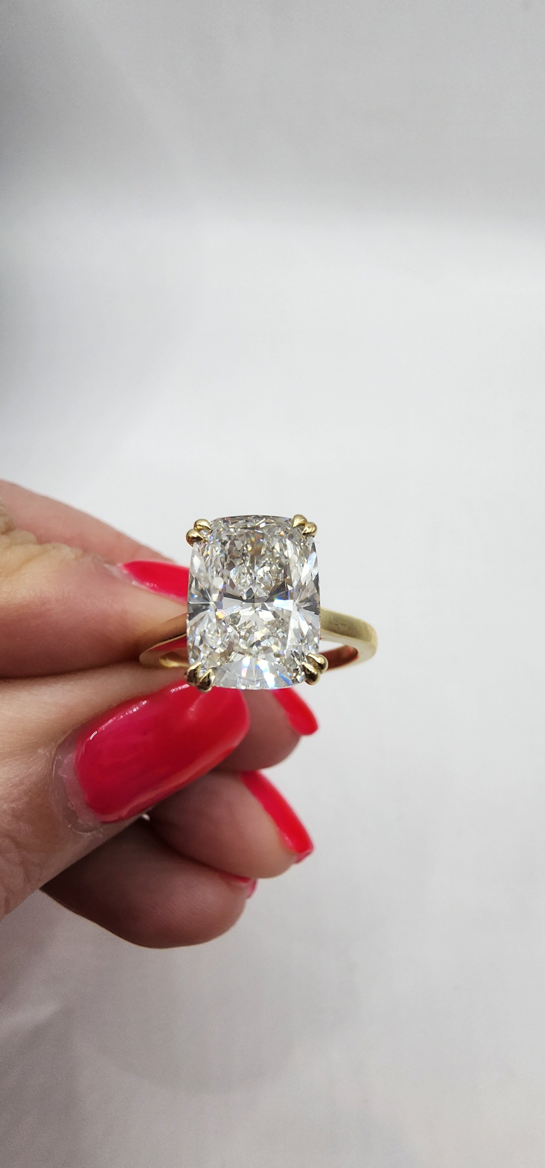 Gold ring with a large diamond held by a hand with red nail polish against a light background