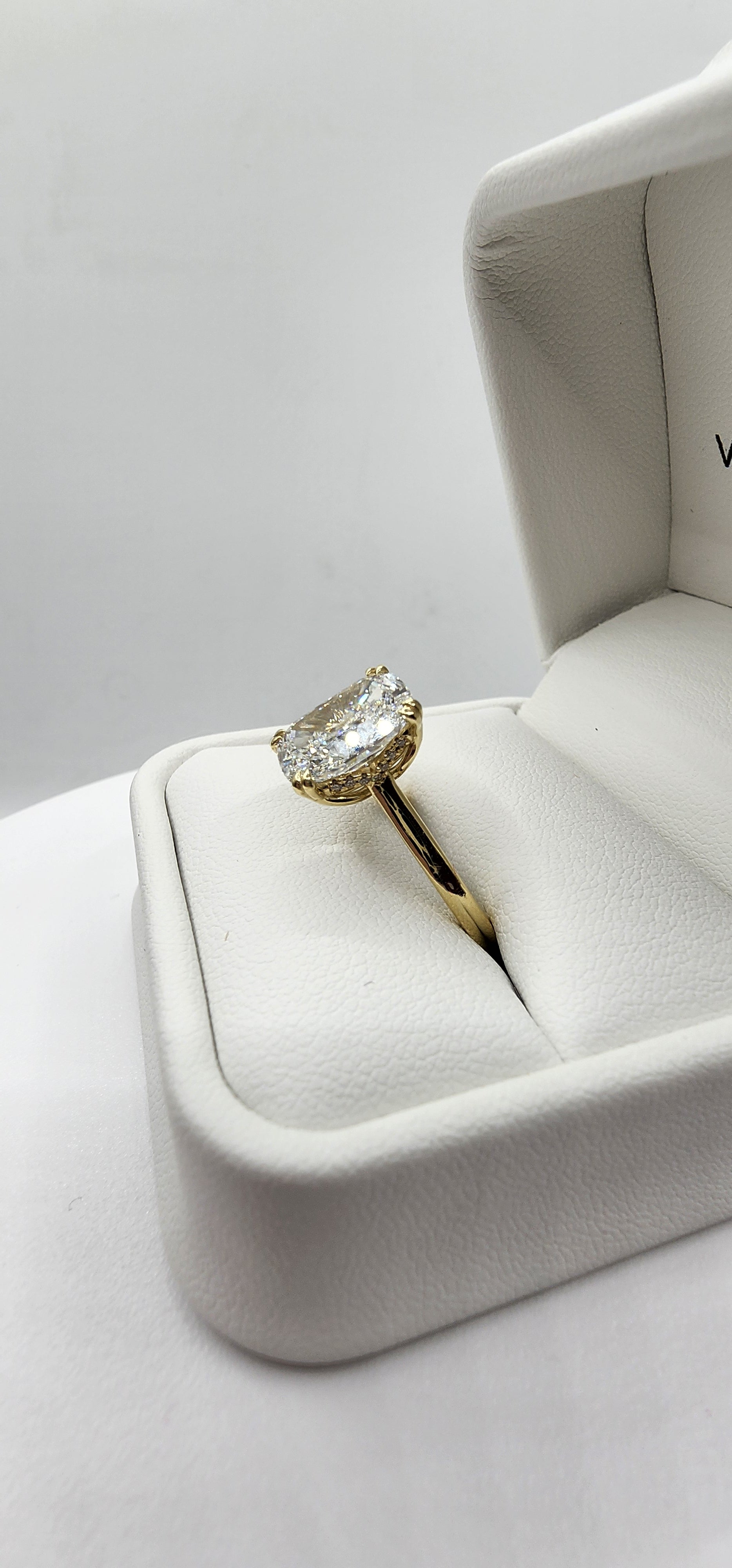 Gold ring with a diamond in a white jewelry box on a light gray background