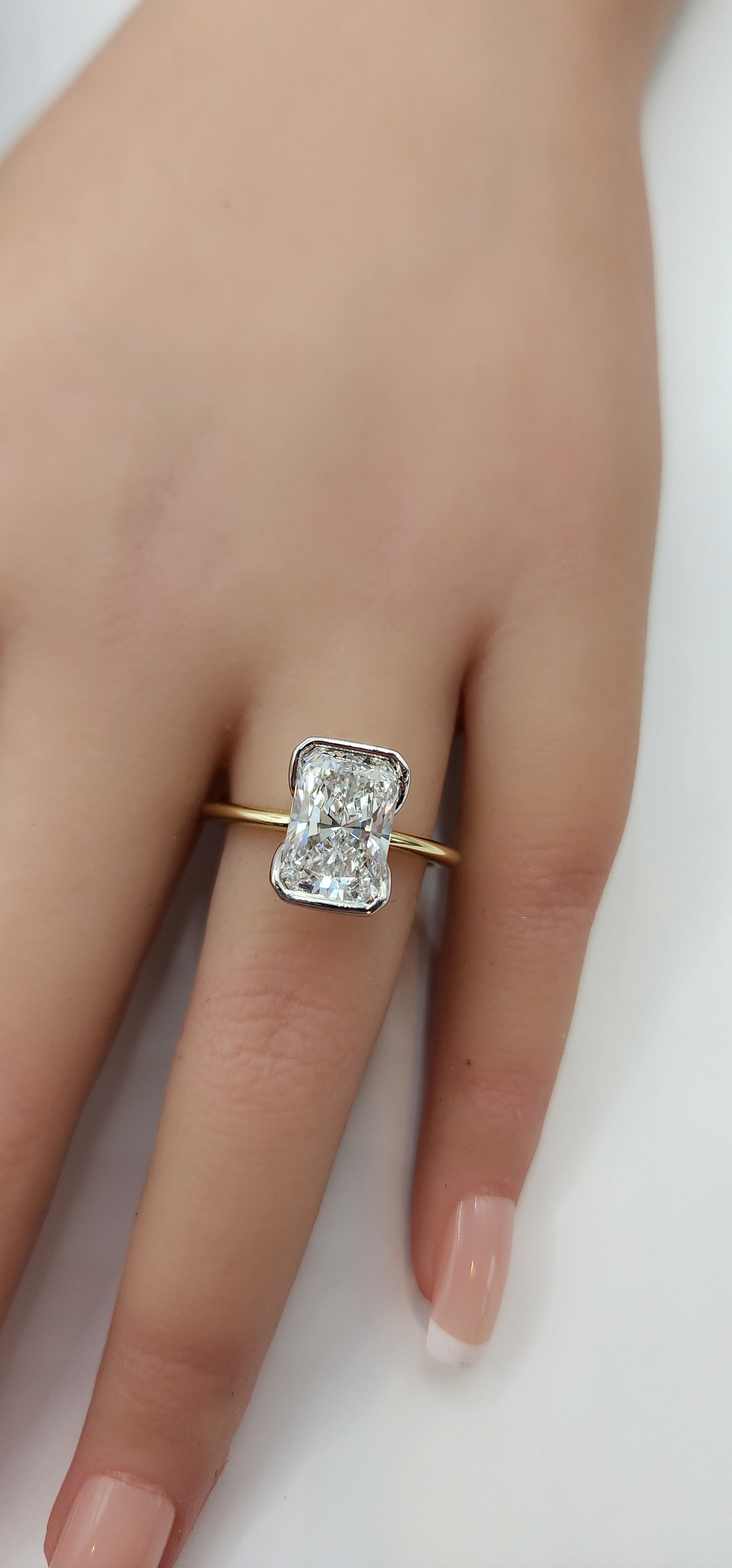 Gold ring with a diamond on a finger against a white background