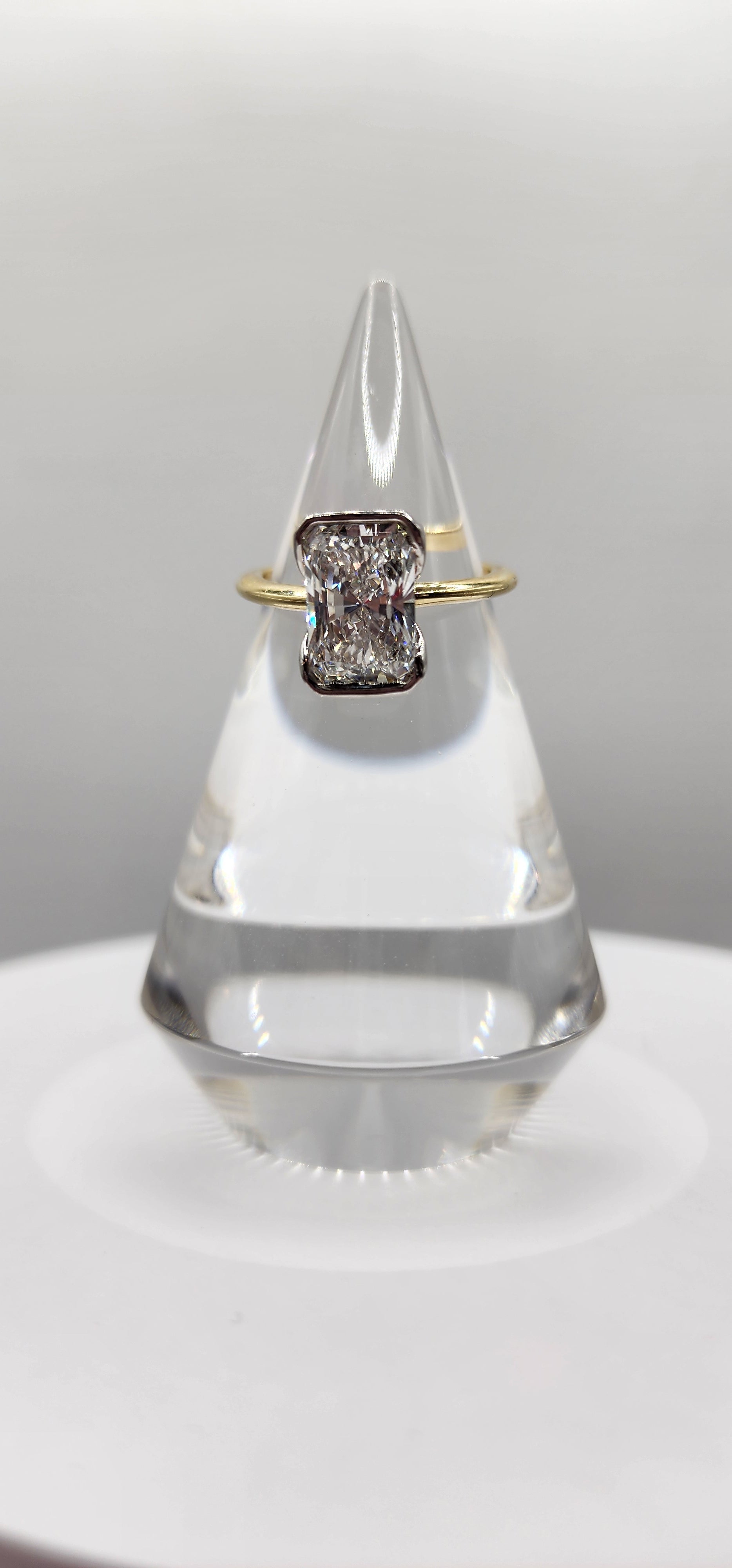 Diamond ring on a clear stand against a light gray background
