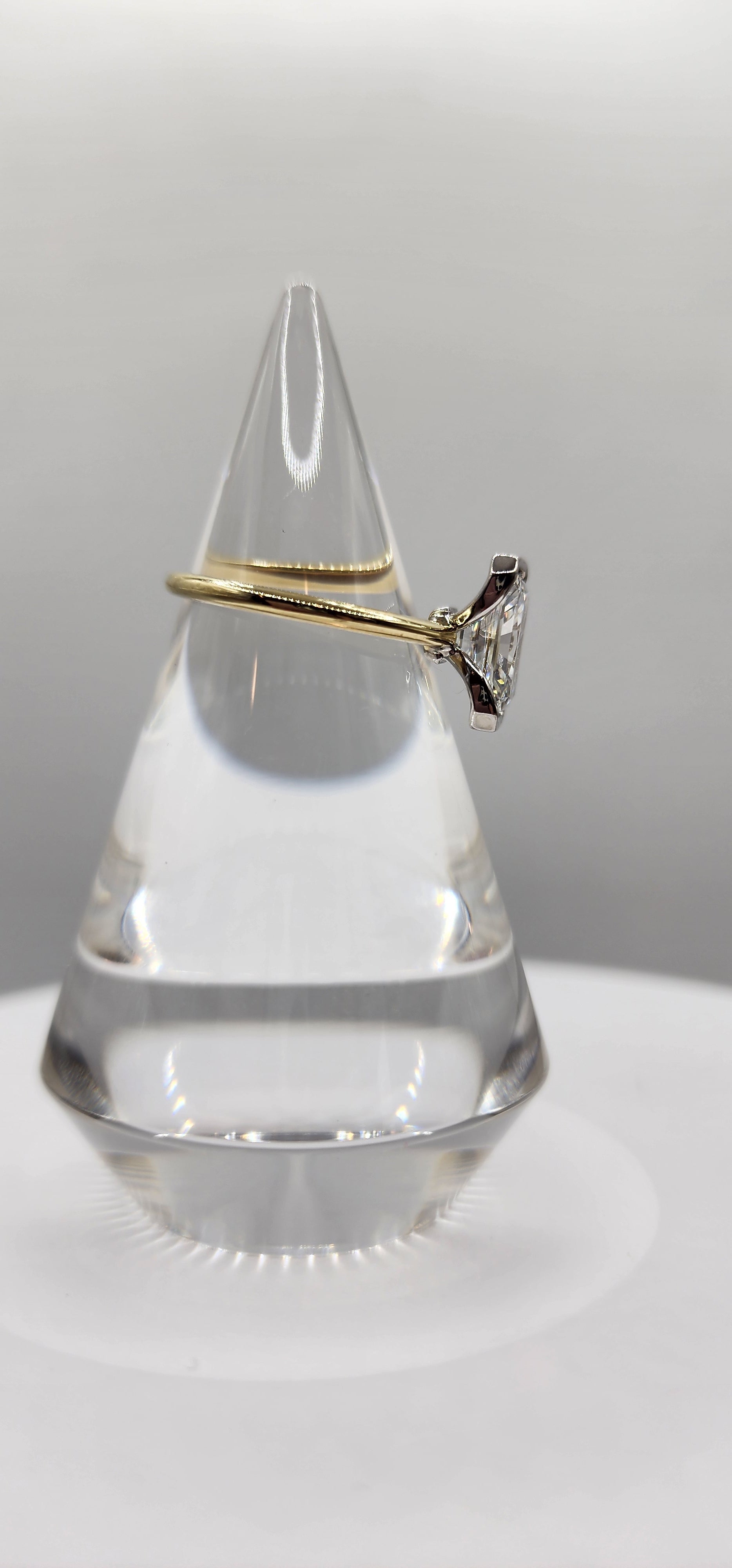 Gold ring on a clear cone against a gray background