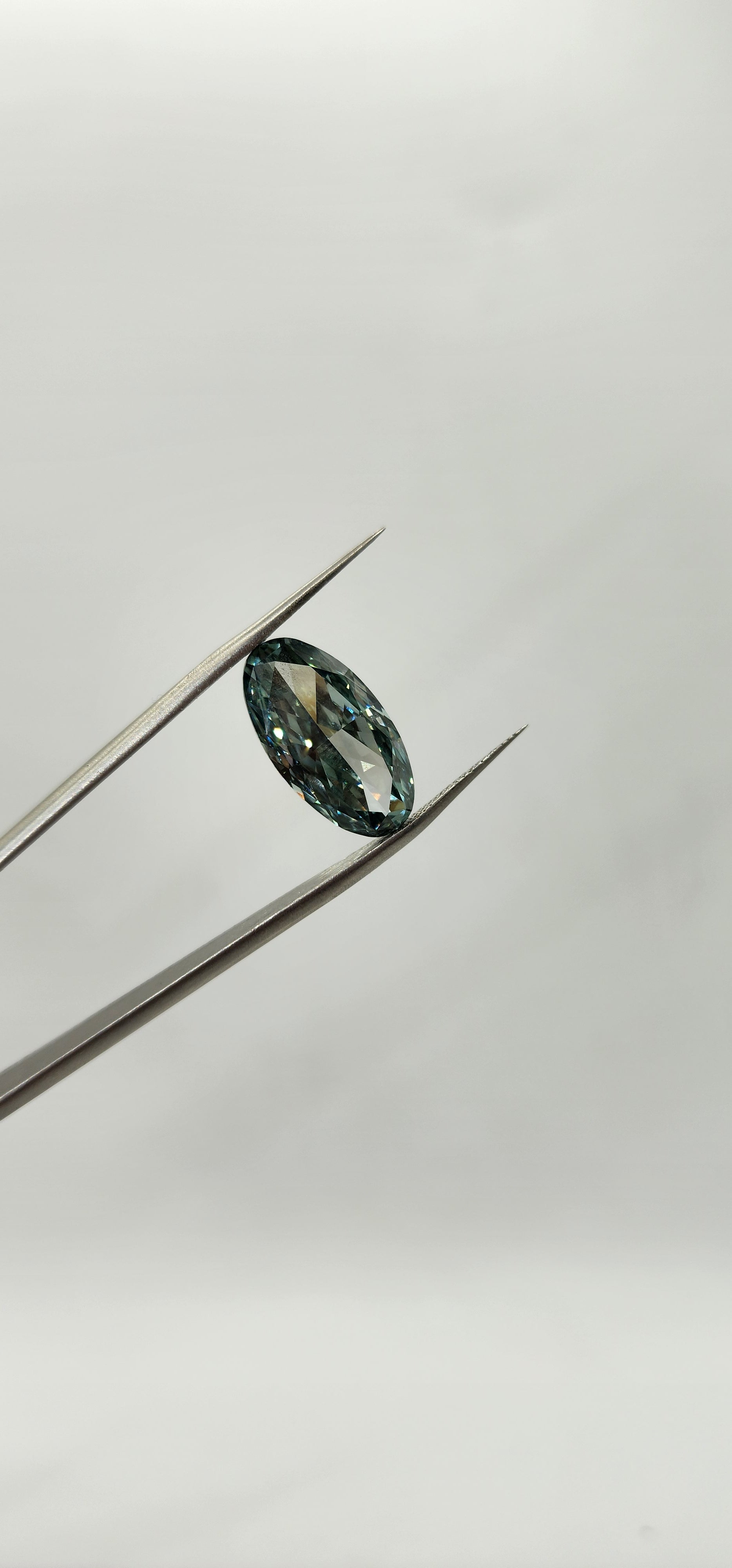 Greenish-blue gemstone on a silver prong against a light gray background