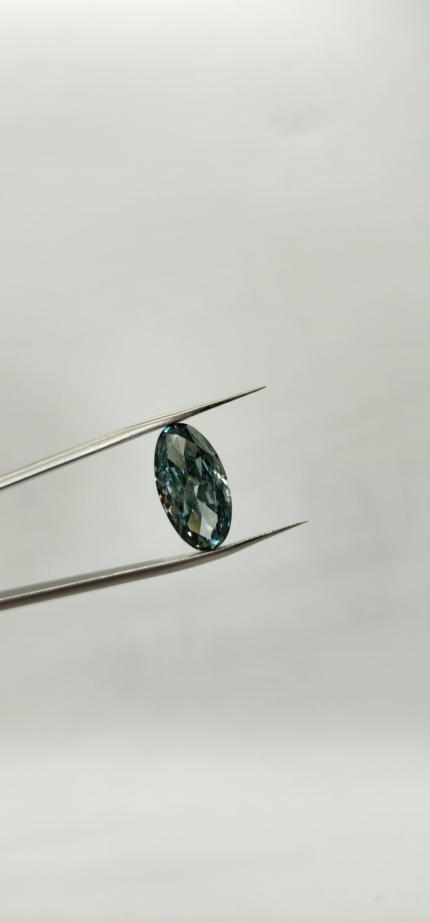 Teal gemstone on a thin metal rod against a light gray background