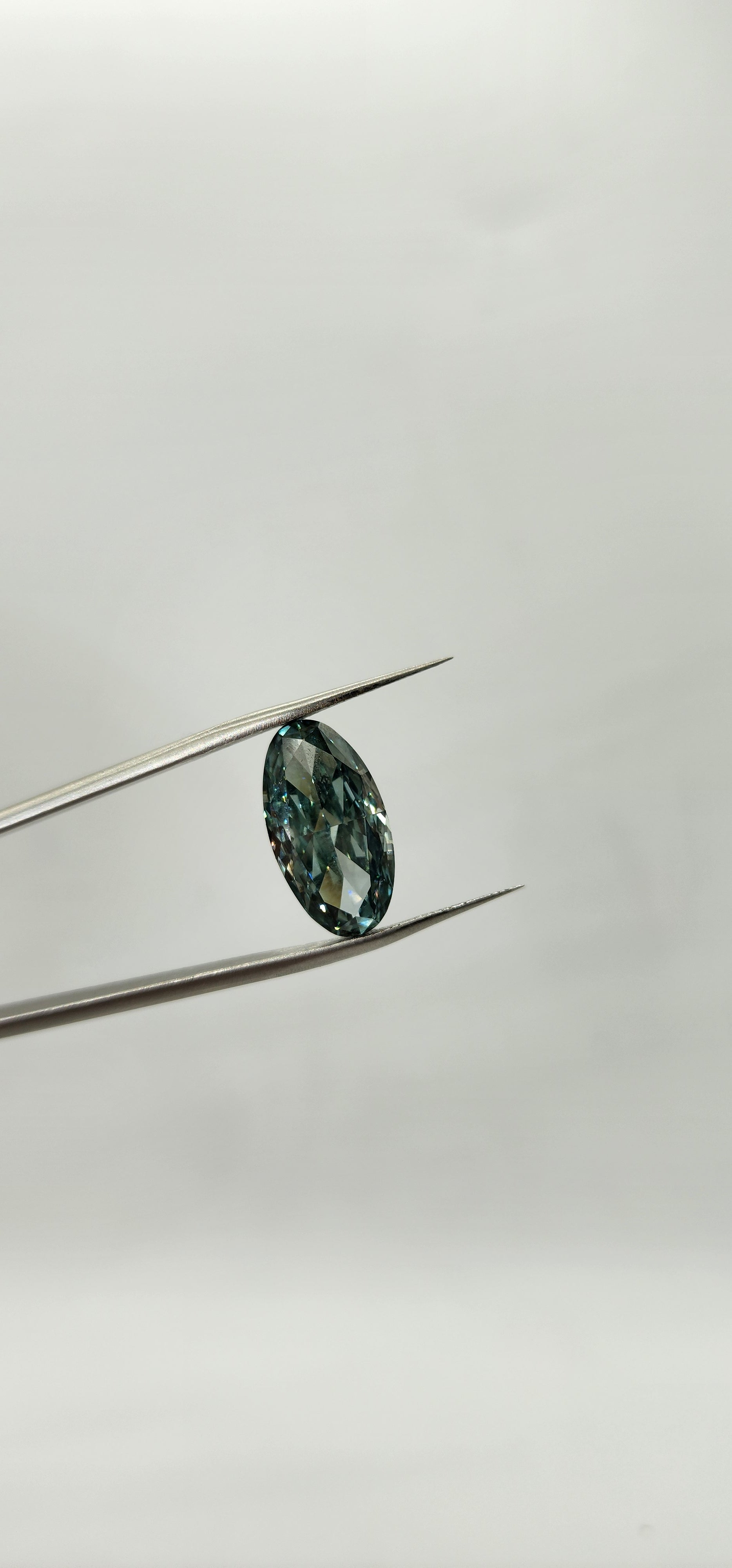 Teal gemstone on a thin metal rod against a light gray background