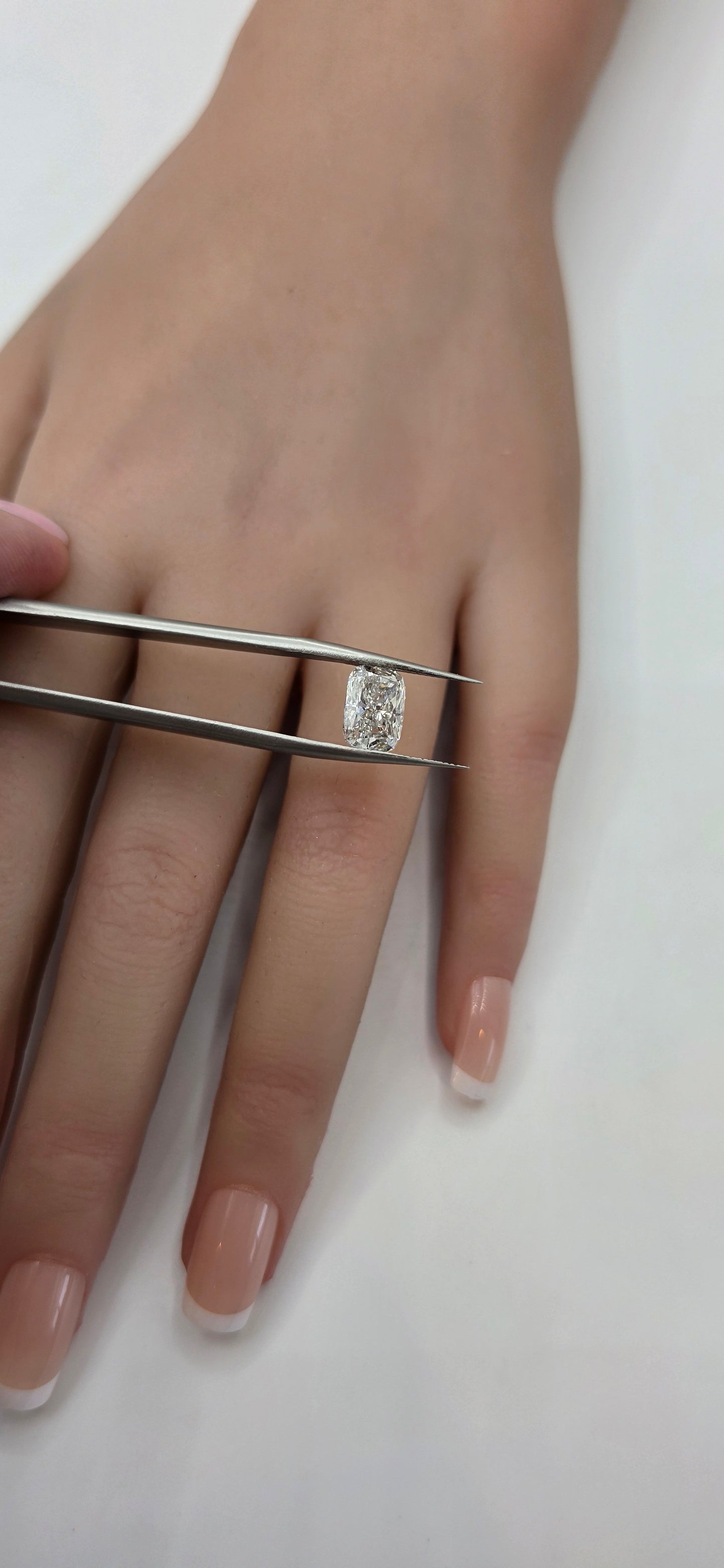 Hand wearing a diamond ring with a pair of tweezers on a white background