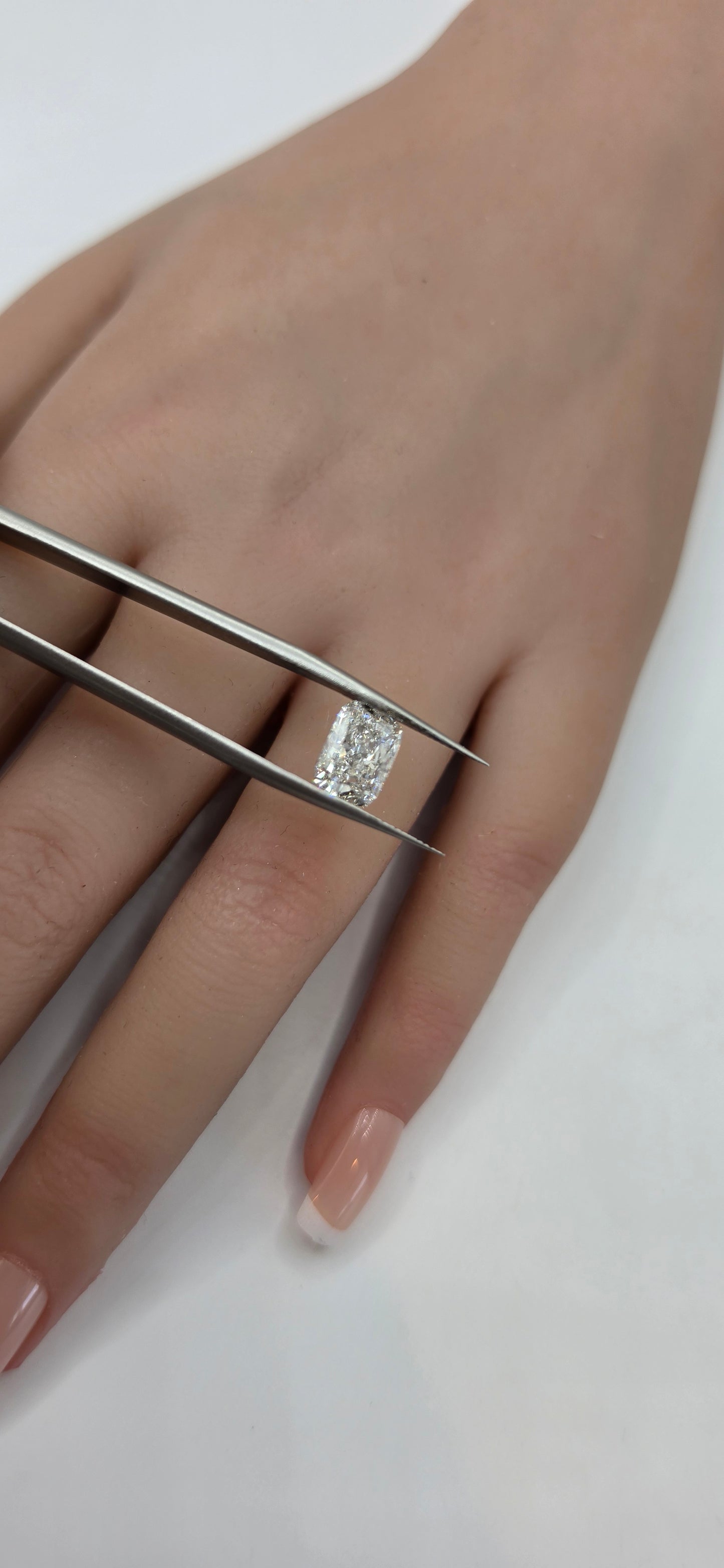 Diamond ring on a finger with tweezers holding it steady against a white background