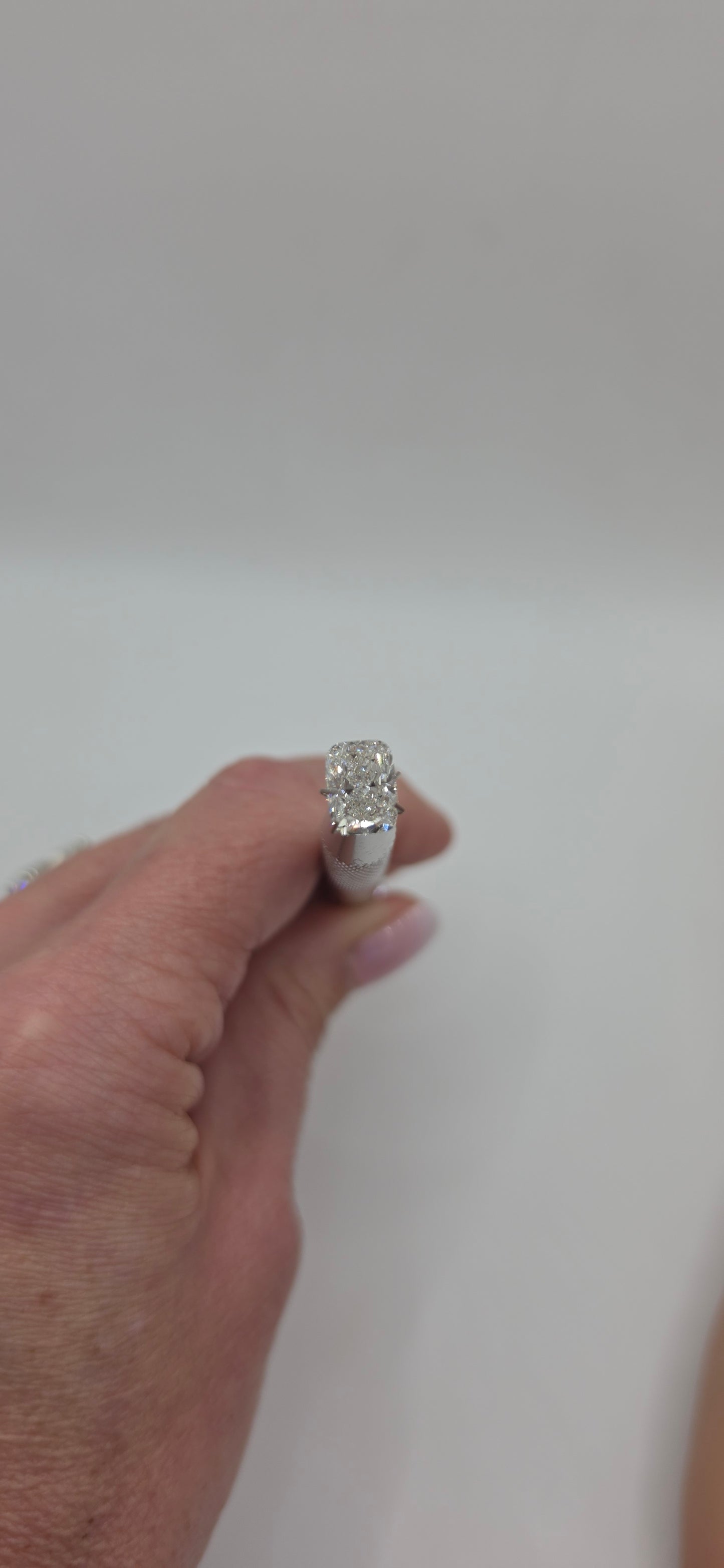 Hand wearing a silver ring with a clear stone on a plain background