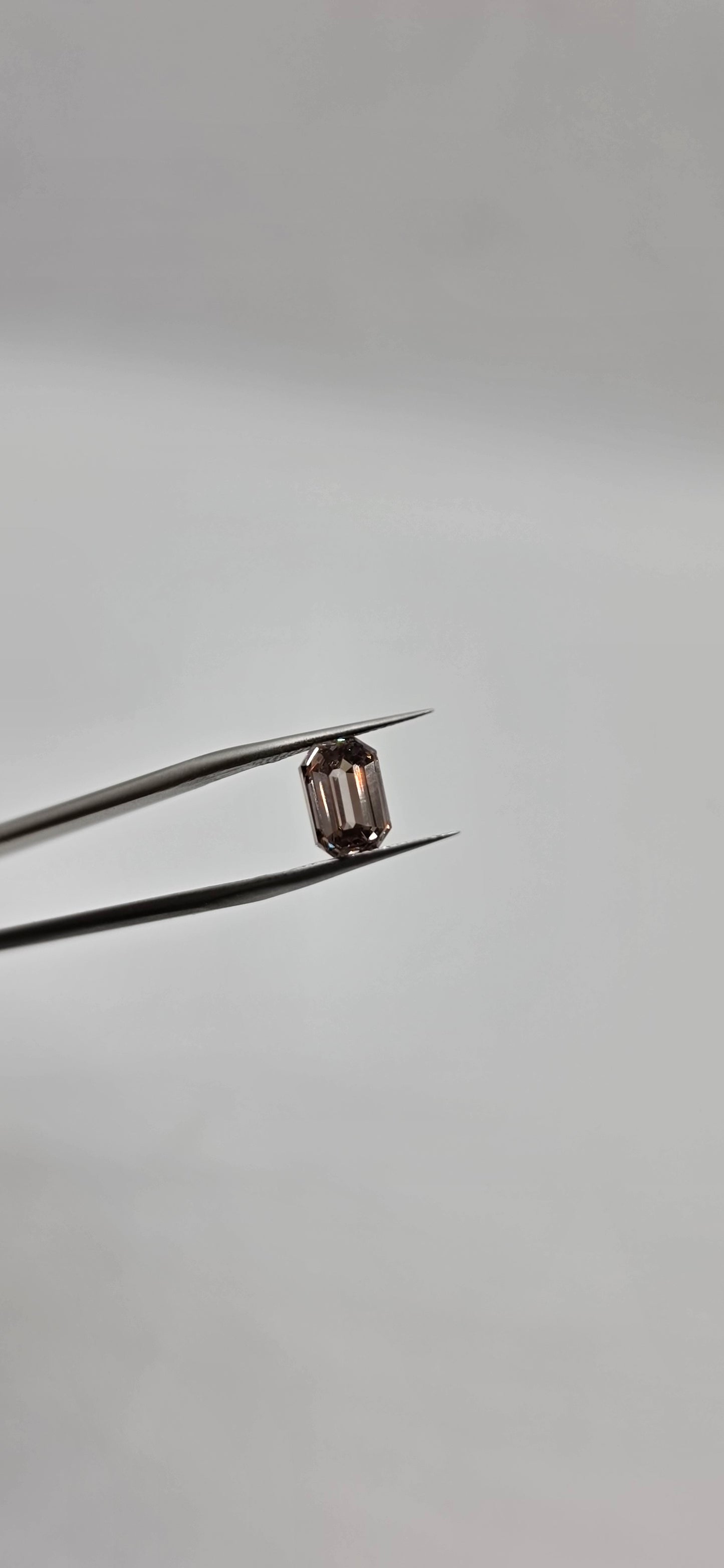 Diamond held between tweezers against a gray background