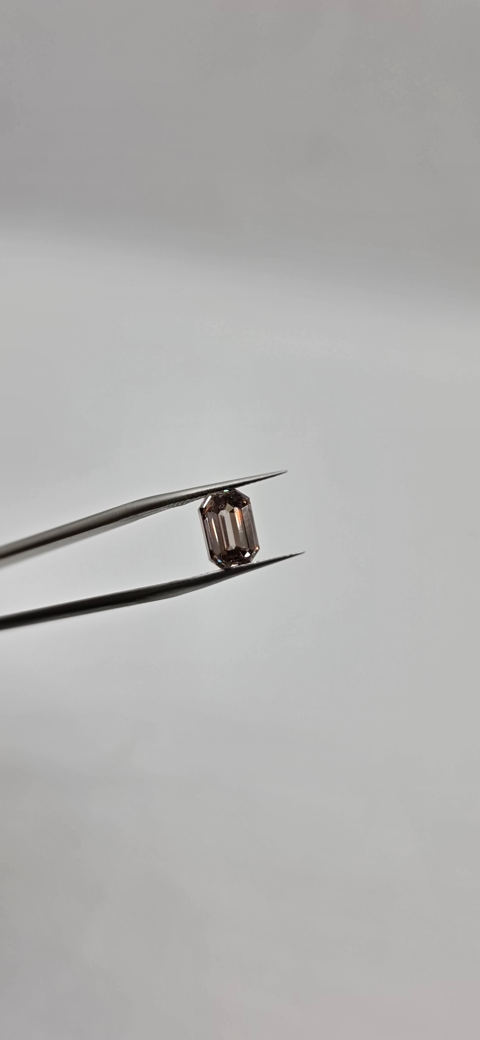 Diamond held between tweezers against a gray background