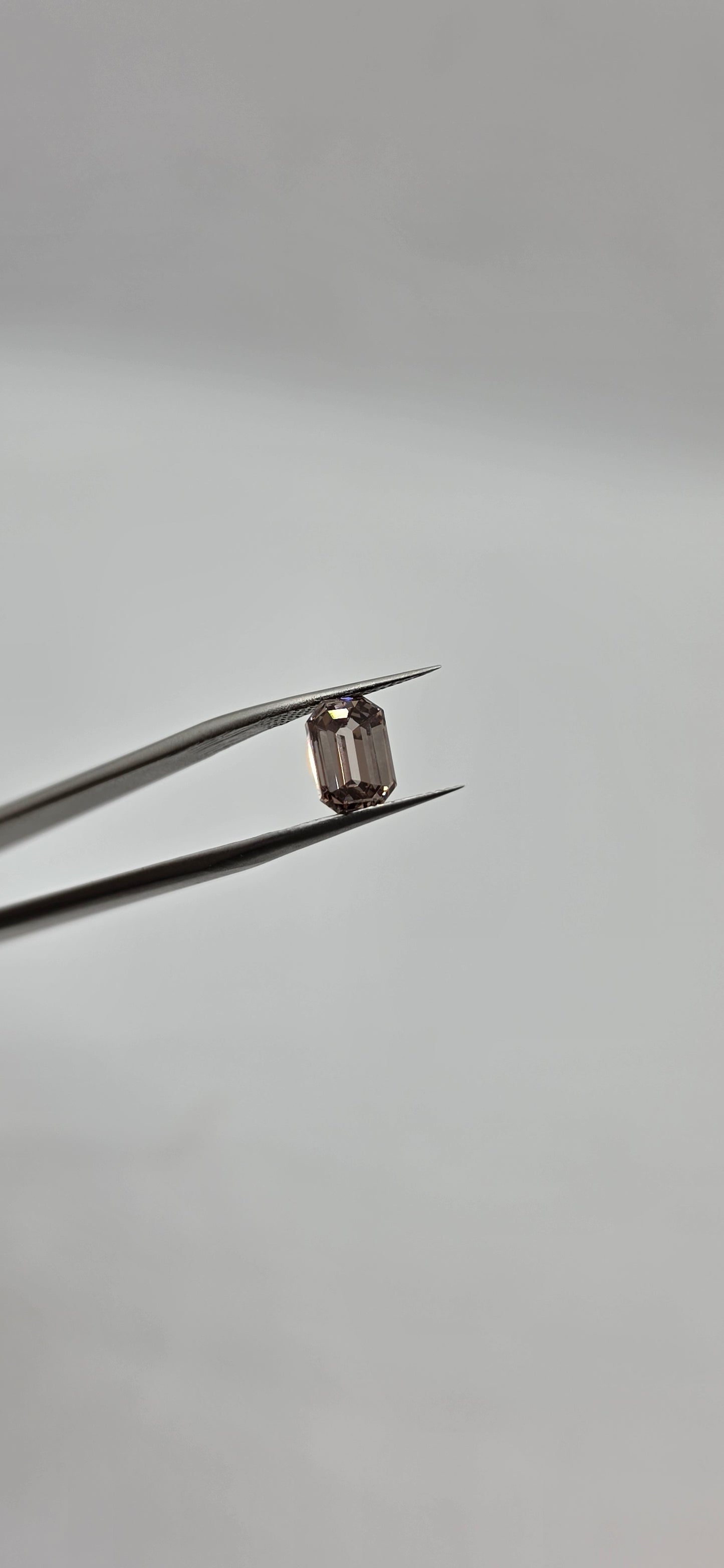 Diamond held between tweezers against a gray background
