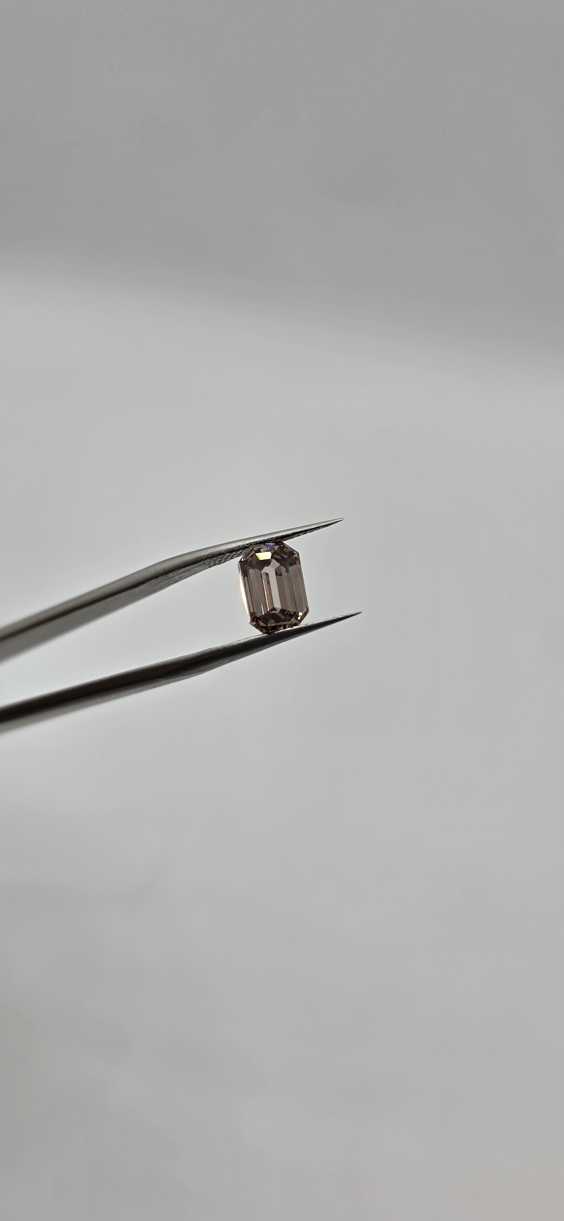 Diamond held between tweezers against a gray background