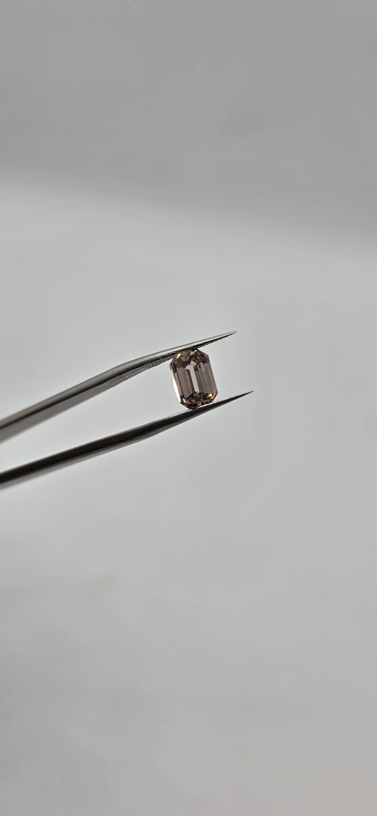 Diamond held between tweezers against a gray background