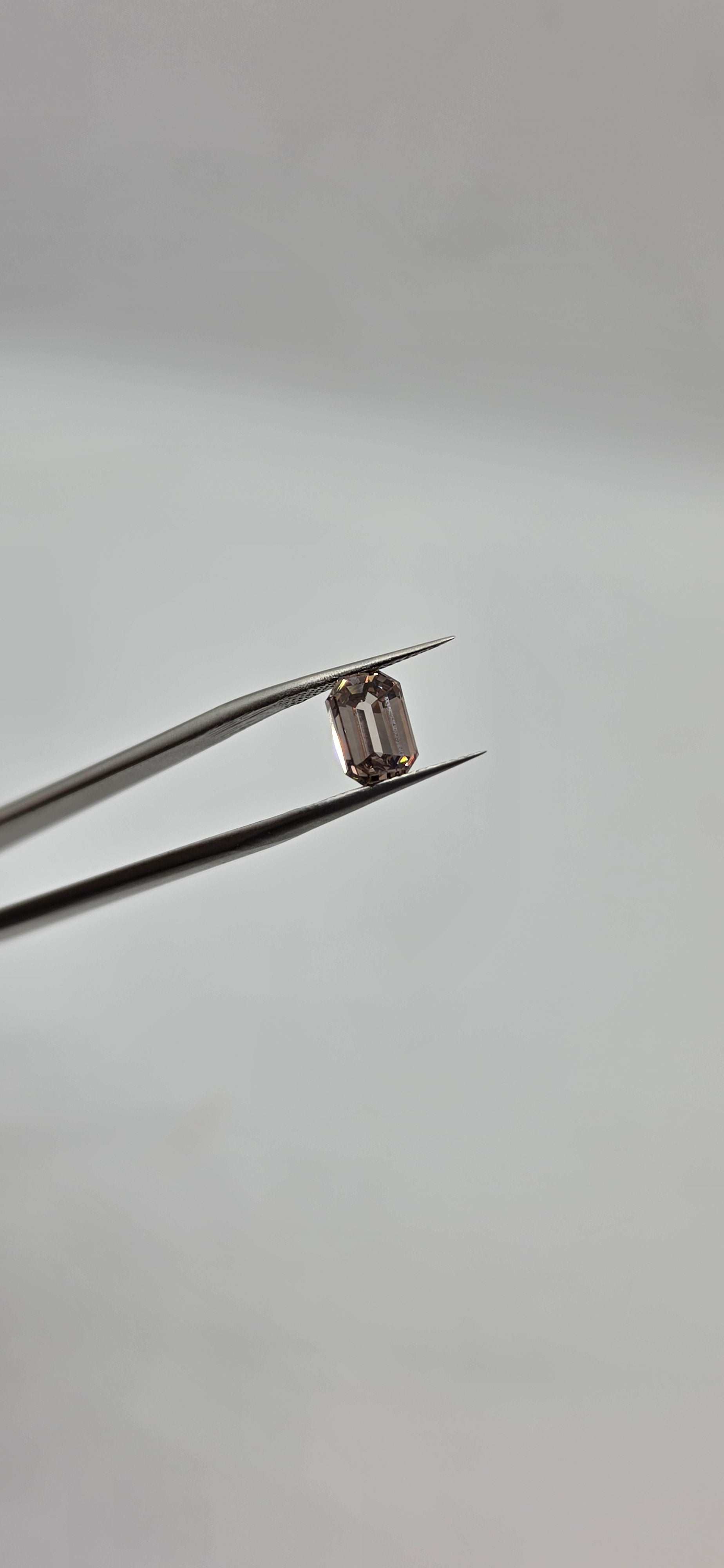 Diamond held between tweezers against a gray background