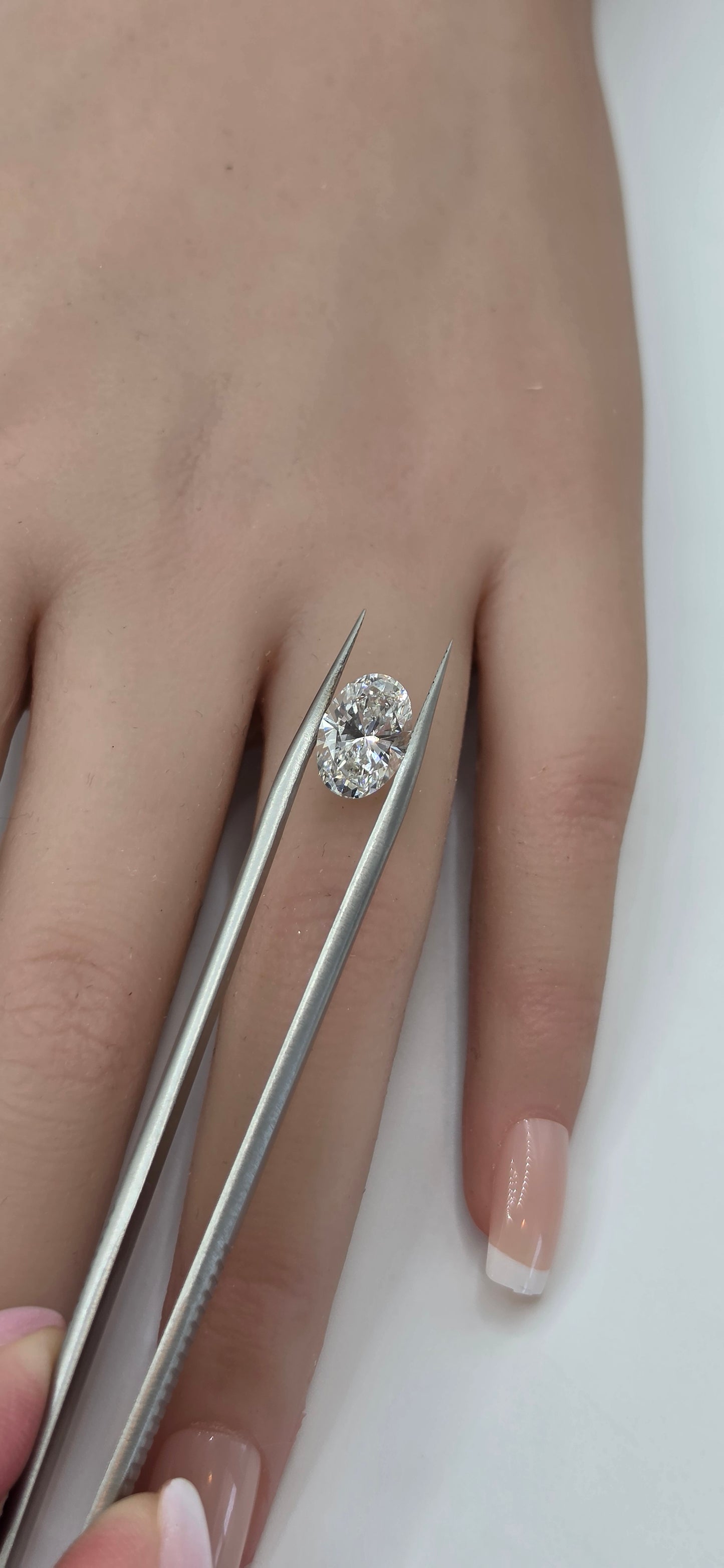 Diamond ring on a finger with tweezers holding it steady against a white background
