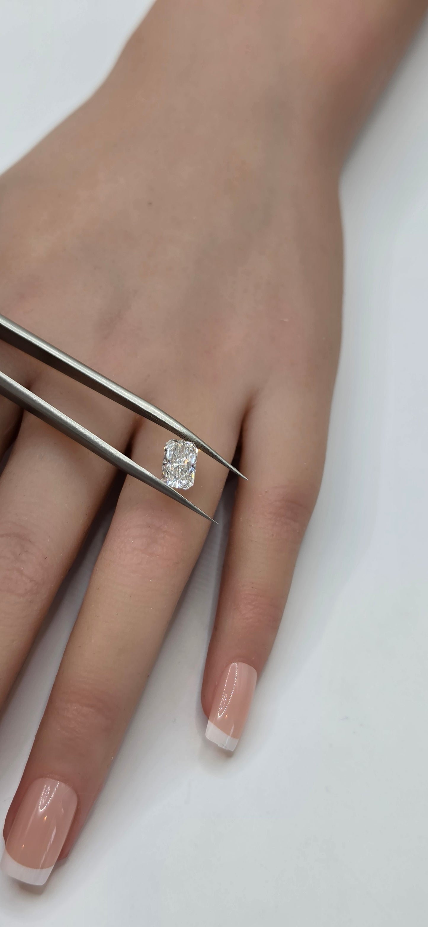 Close-up of a hand with a diamond ring being adjusted with tweezers on a white background