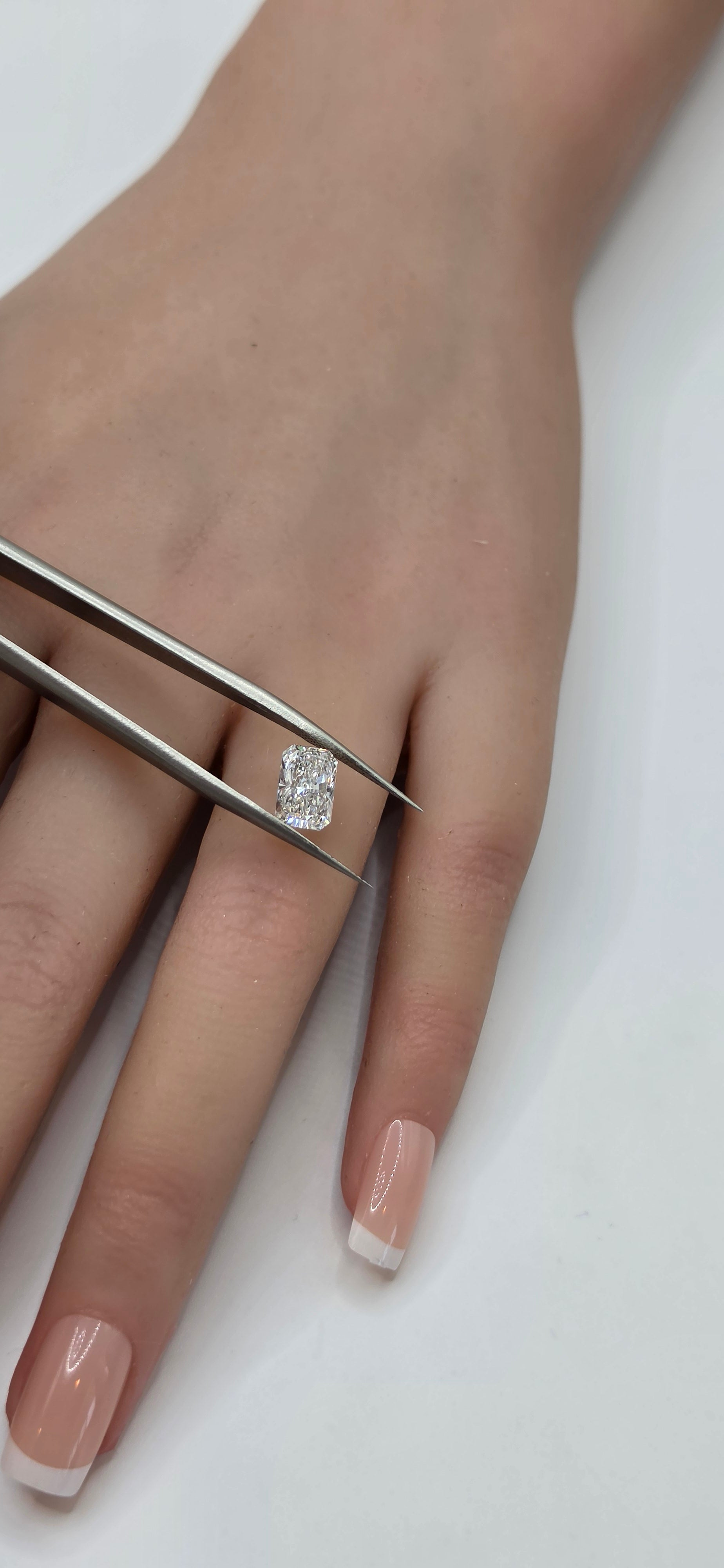 Hand with a diamond ring being adjusted with tweezers on a white background