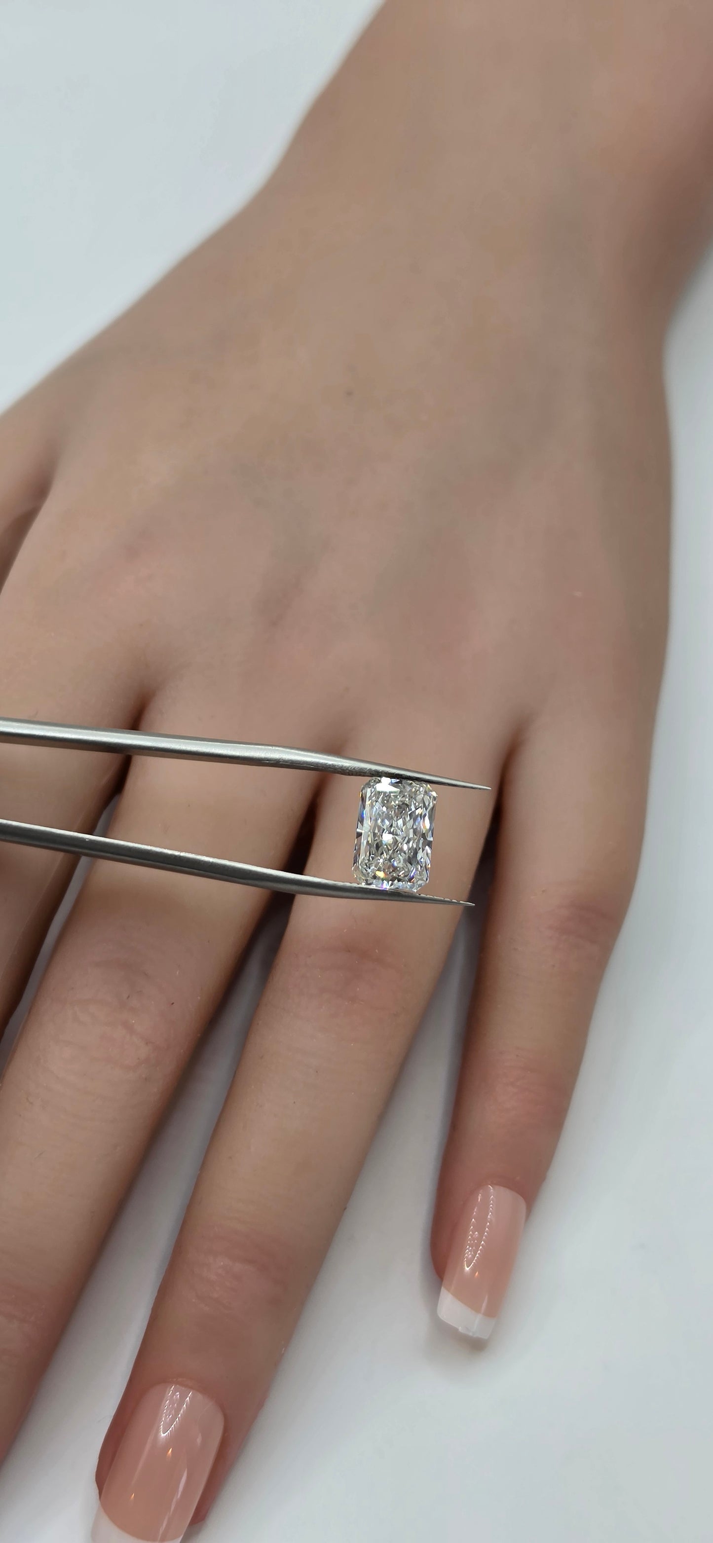 Hand wearing a diamond ring with tweezers adjusting it on a white background