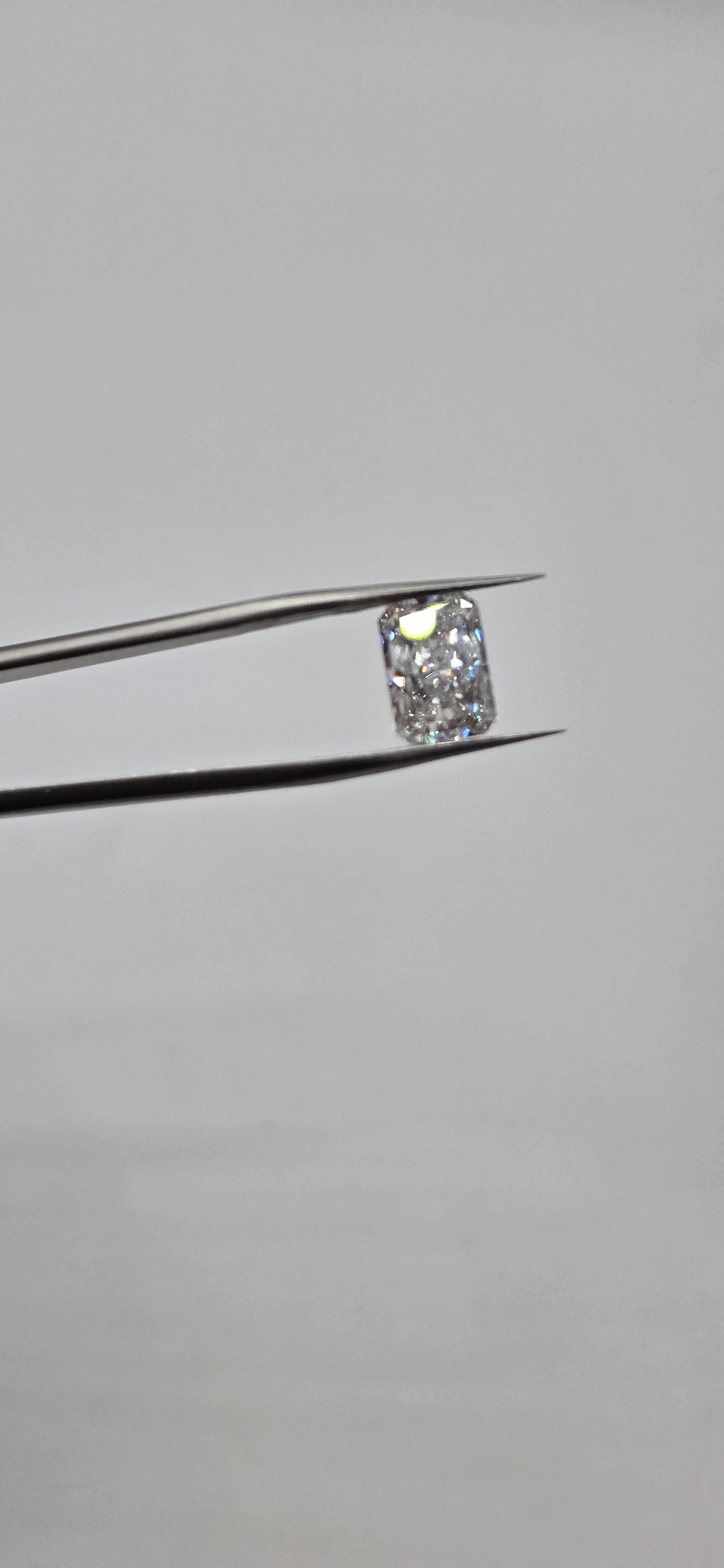 Diamond held between tweezers against a gray background